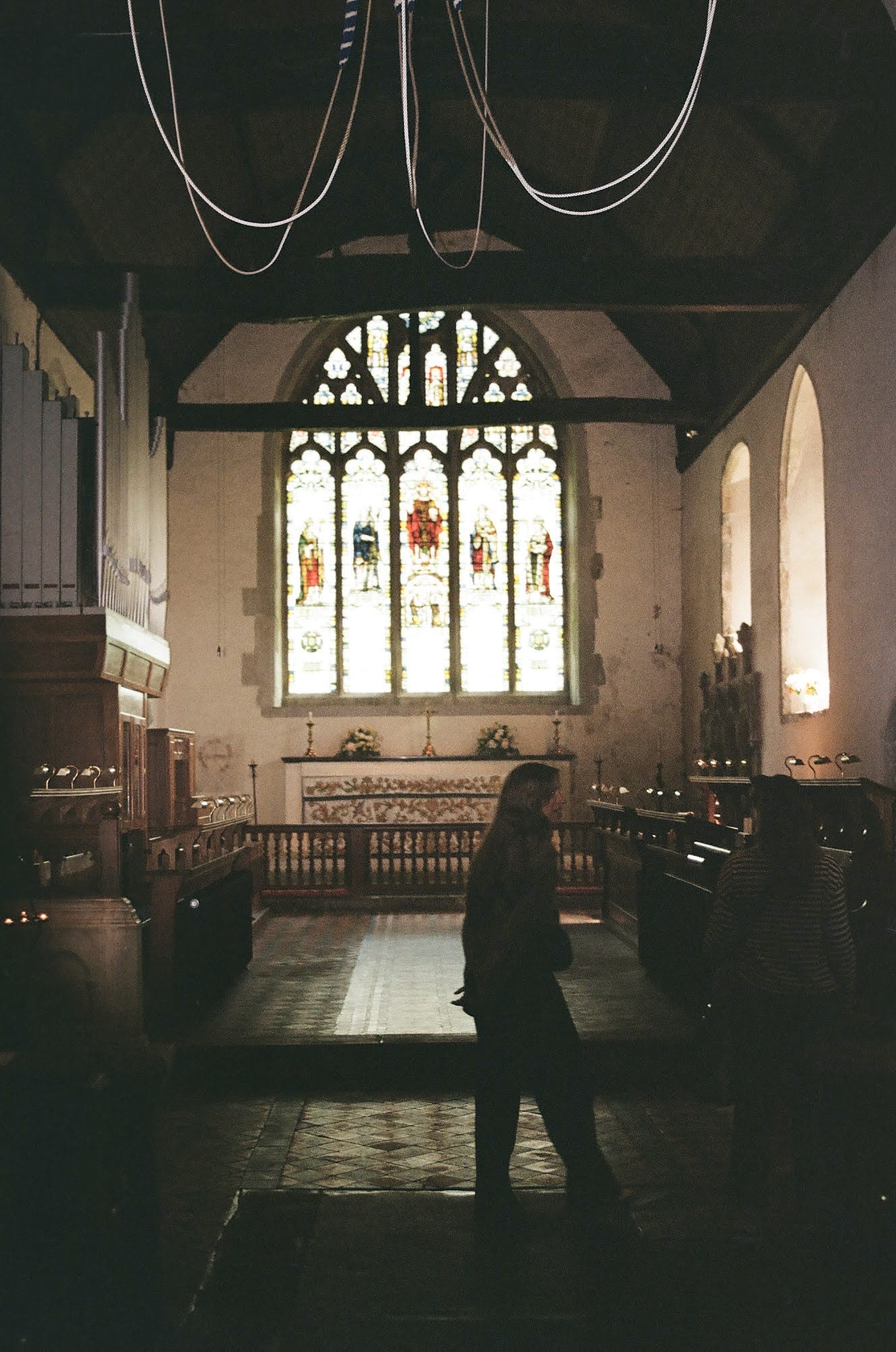 Inside a church with stained glass windows, wooden pews, and a woman standing near the aisle.