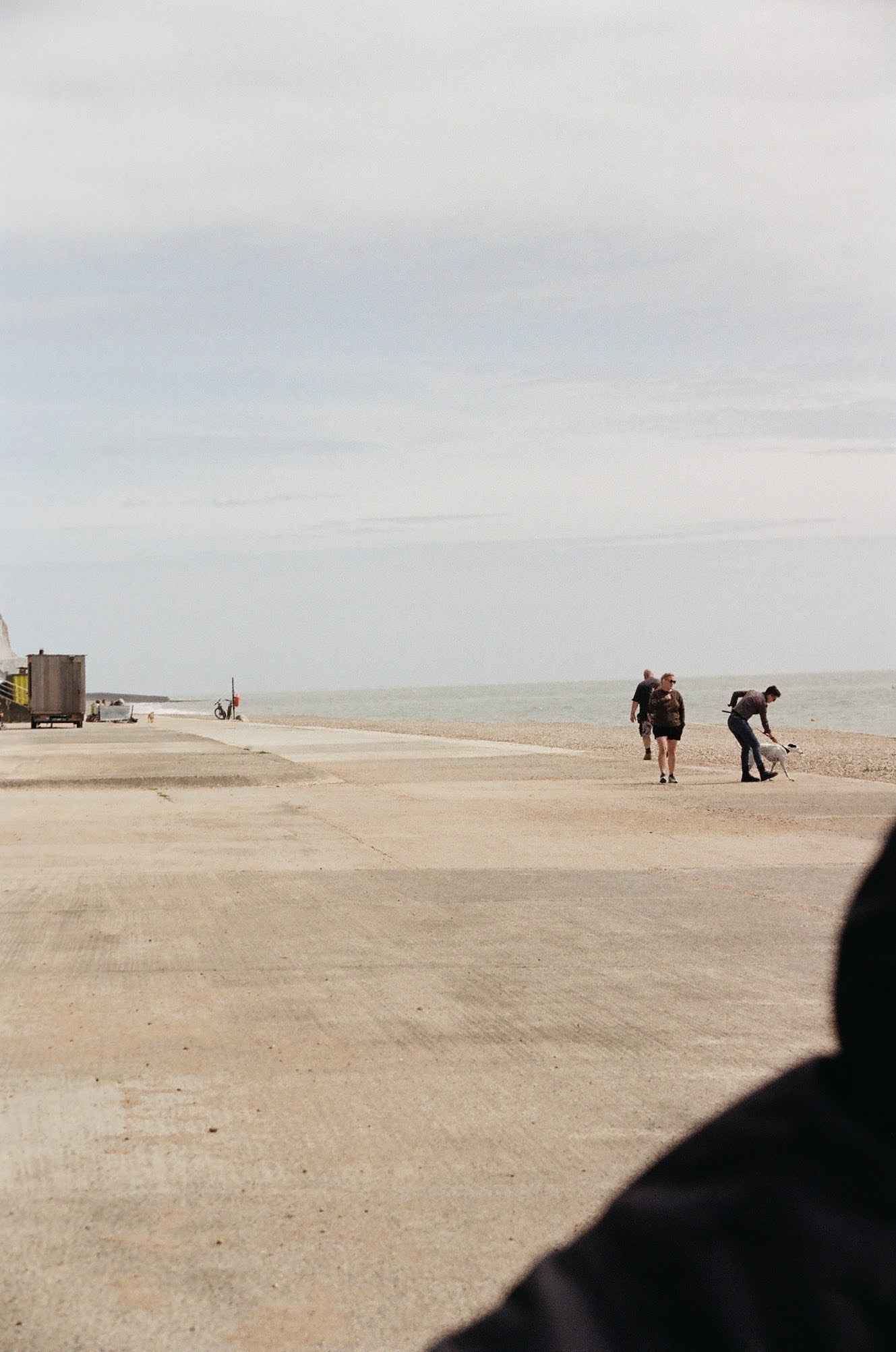 People walking on a beach near the water, with a cloudy sky overhead.