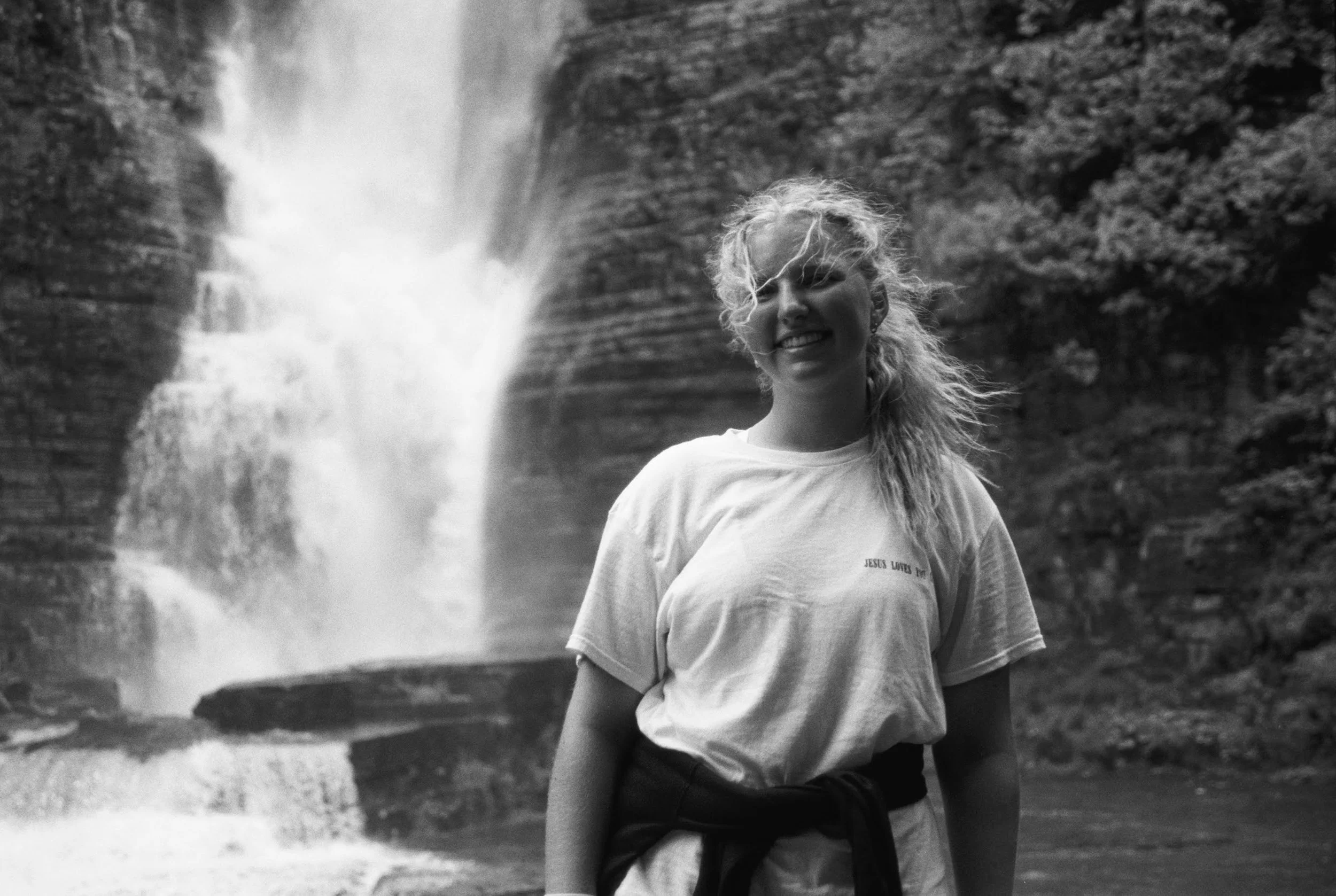 A woman with curly hair smiling and standing outdoors near a waterfall.