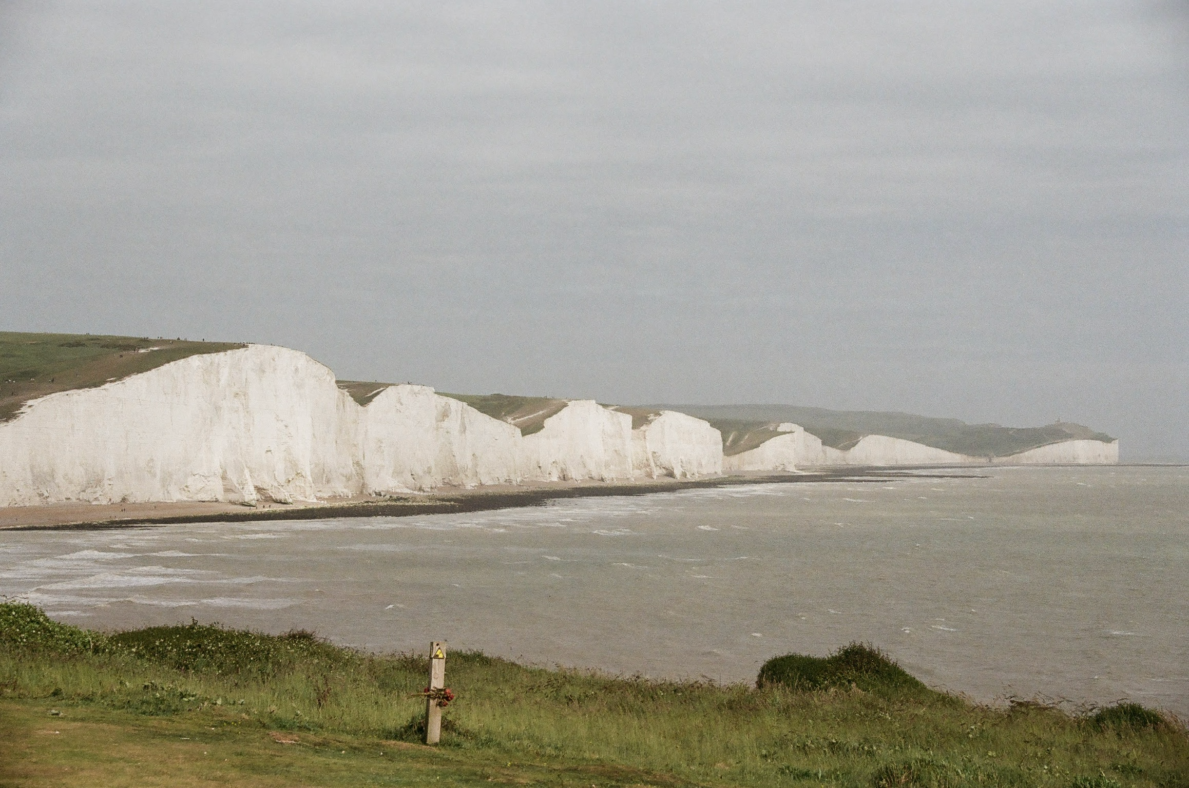 White chalk cliffs along a shoreline with grassy areas and a cloudy sky overhead.