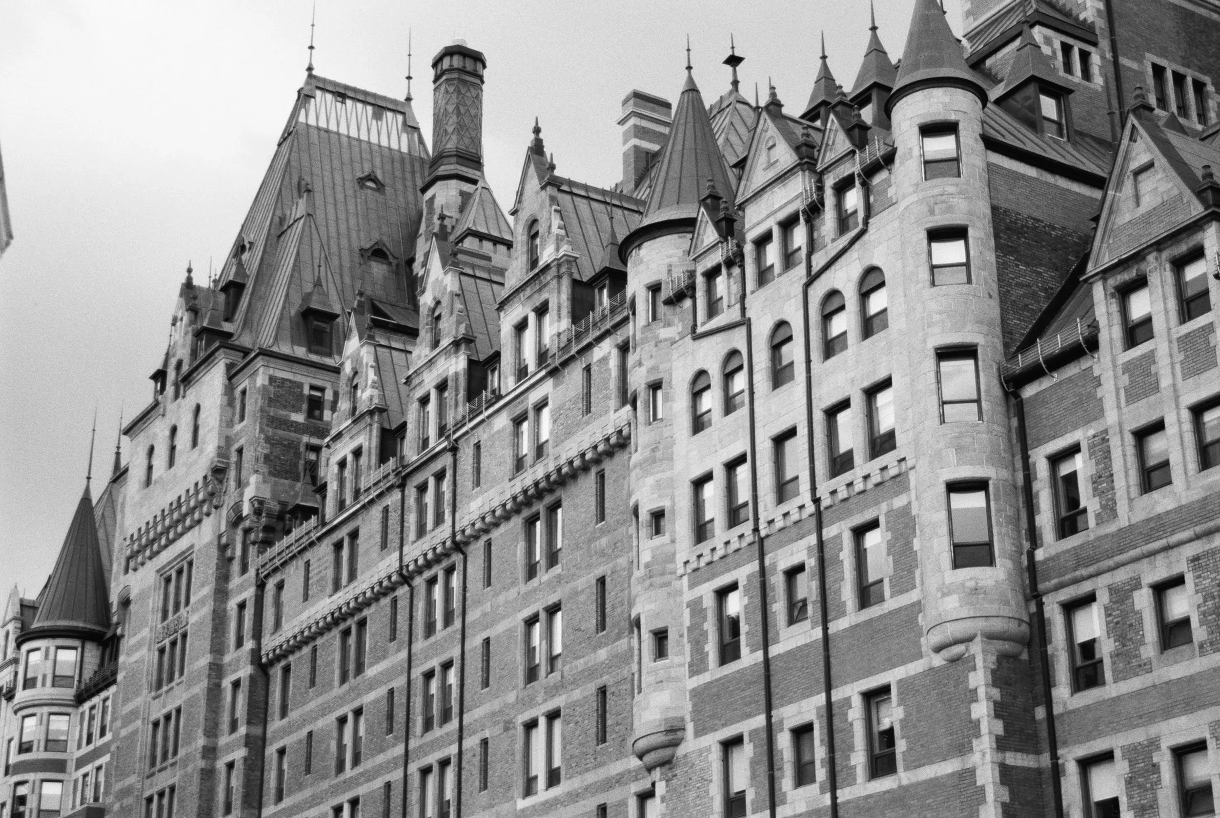 Black and white photograph of a historic, ornate building with multiple peaked roofs, turrets, and arched windows, showcasing Gothic Revival architecture.