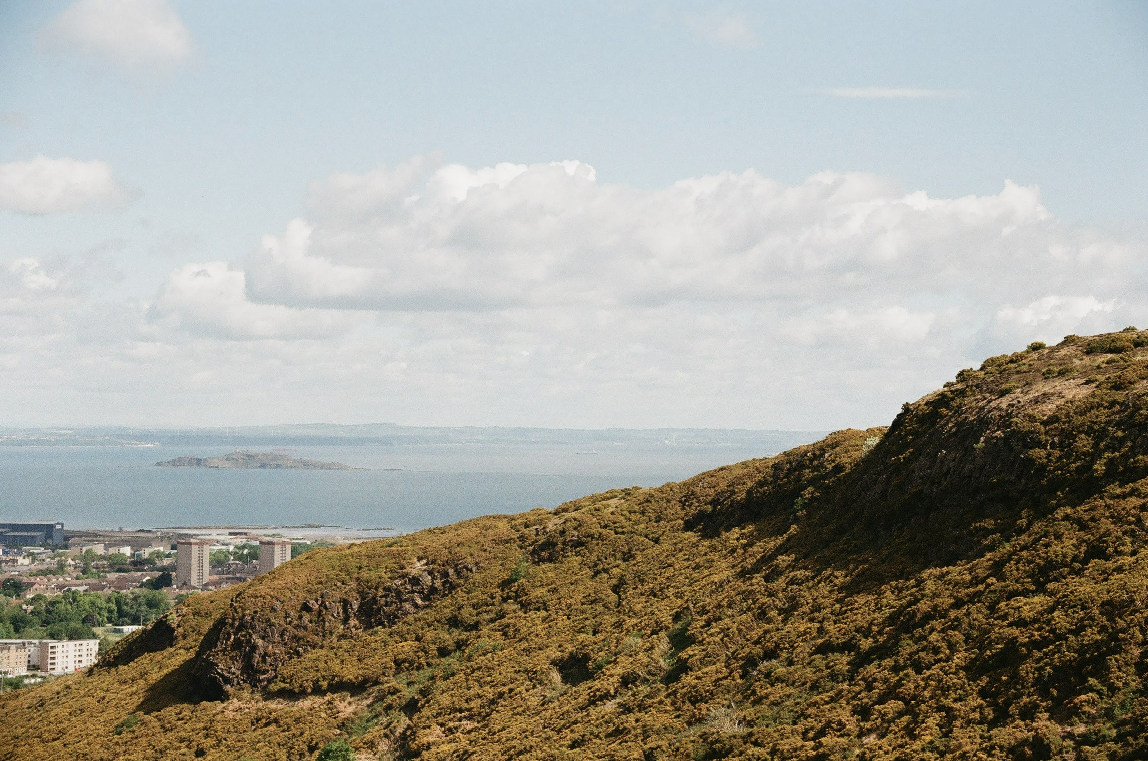 Hilly landscape with a city and water in the distance, under a partly cloudy sky.