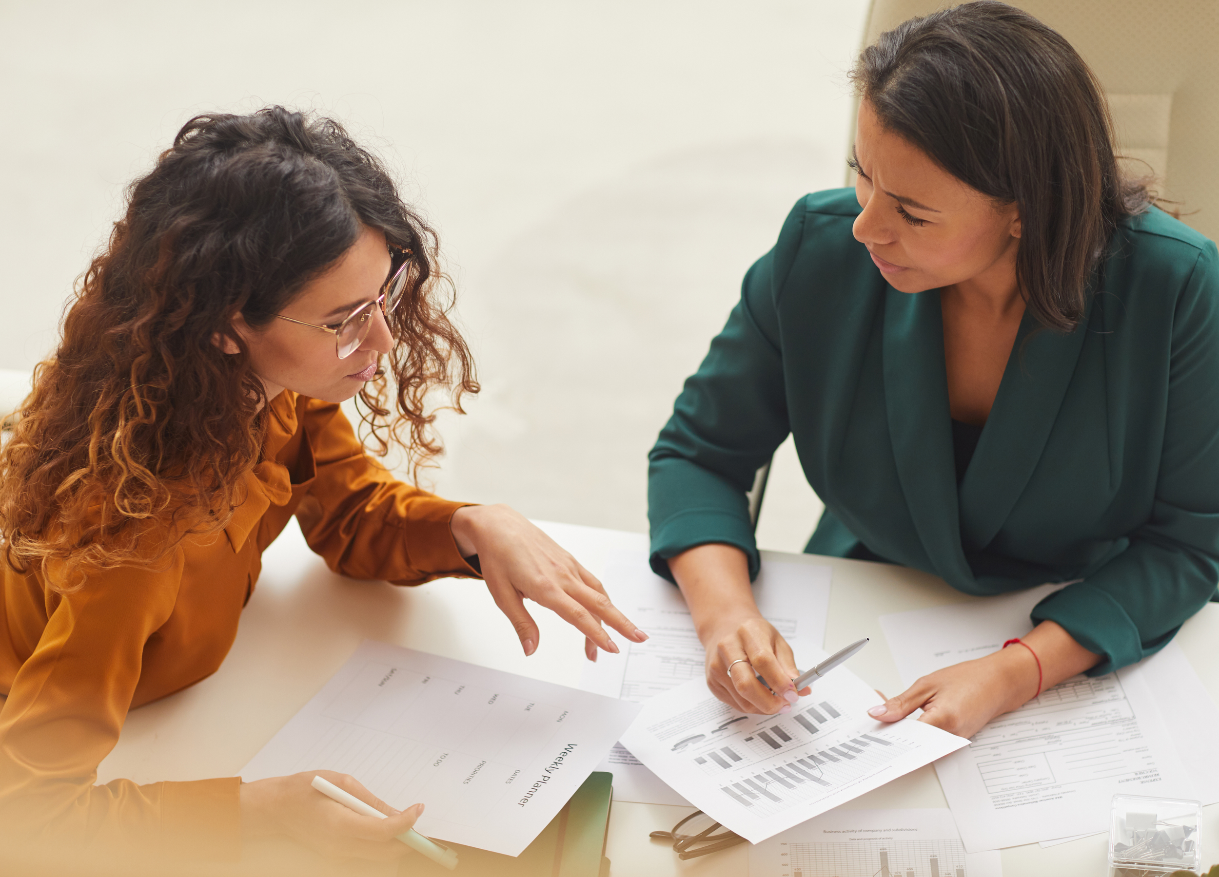 Small business owner and business advisor discussing financial documents and graphs at a table in an office setting.