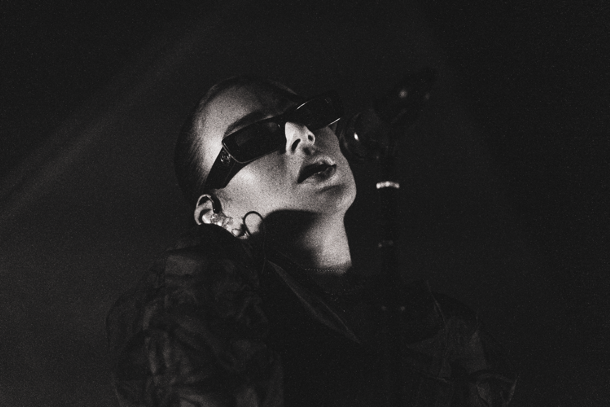 Black and white photo of a performer with slicked-back hair and wearing dark sunglasses, singing into a microphone.