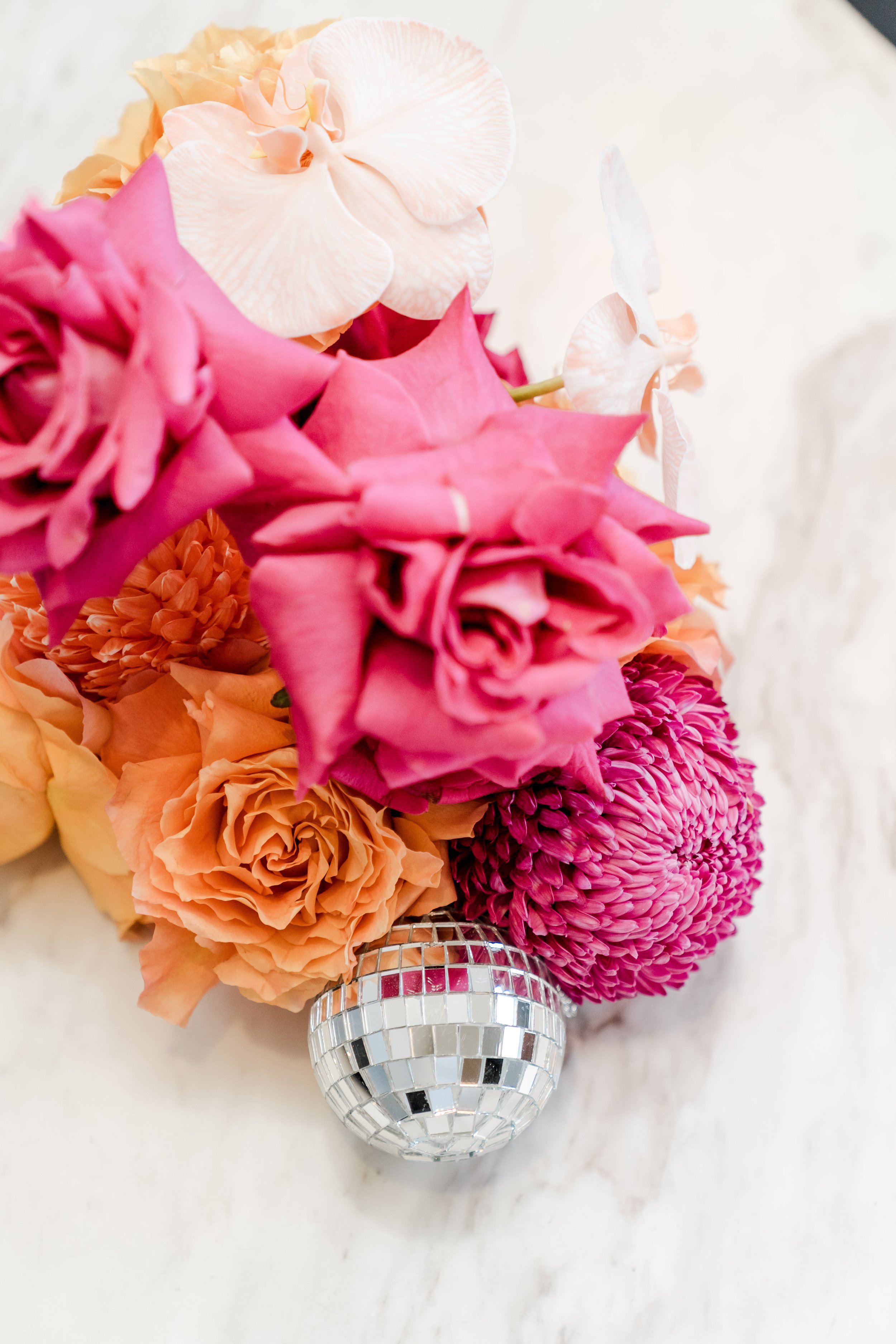 Close-up of a bouquet of pink, peach, and cream flowers in front of a small disco ball