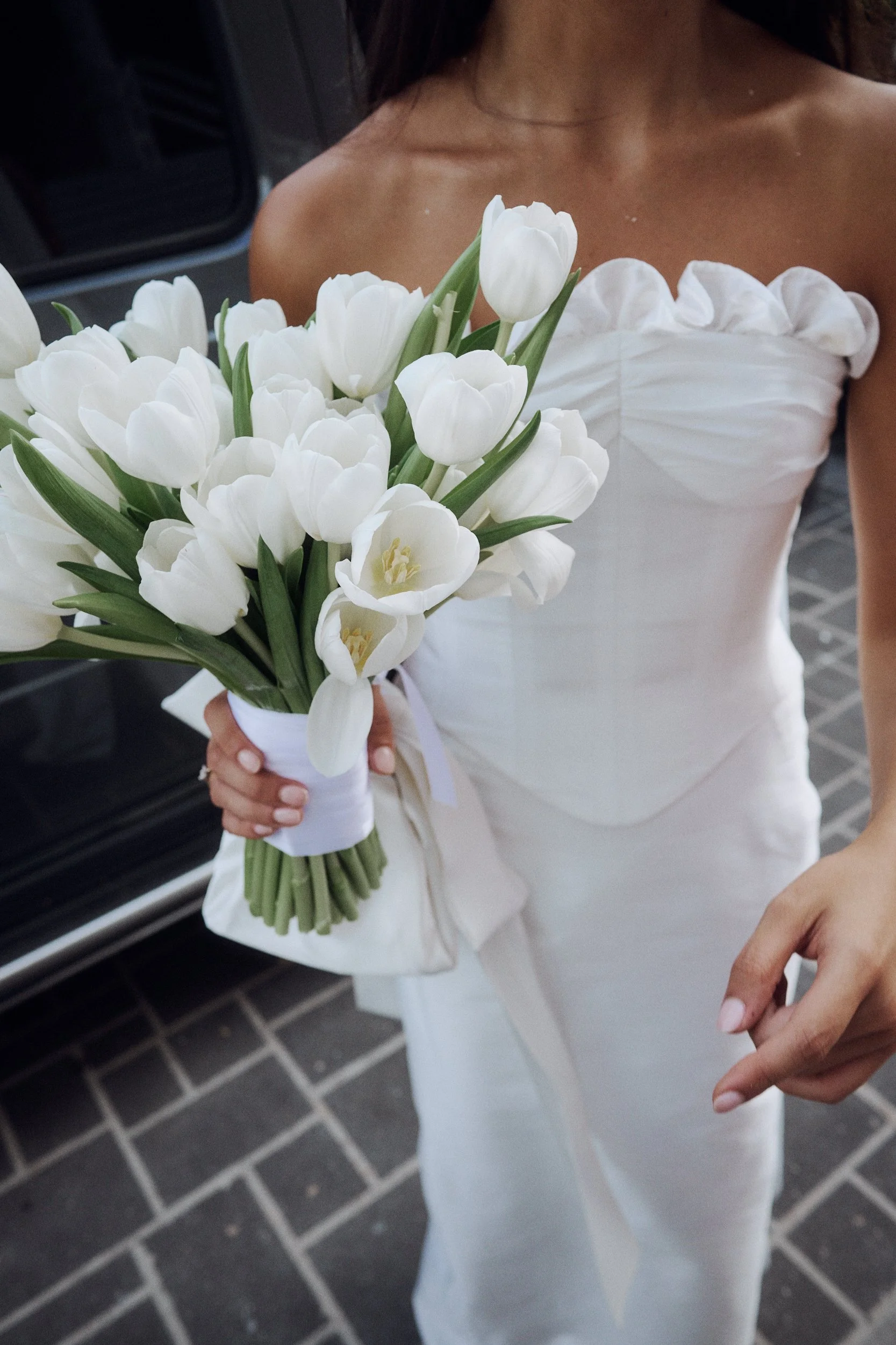 A woman in a white strapless dress holding a bouquet of white tulips.