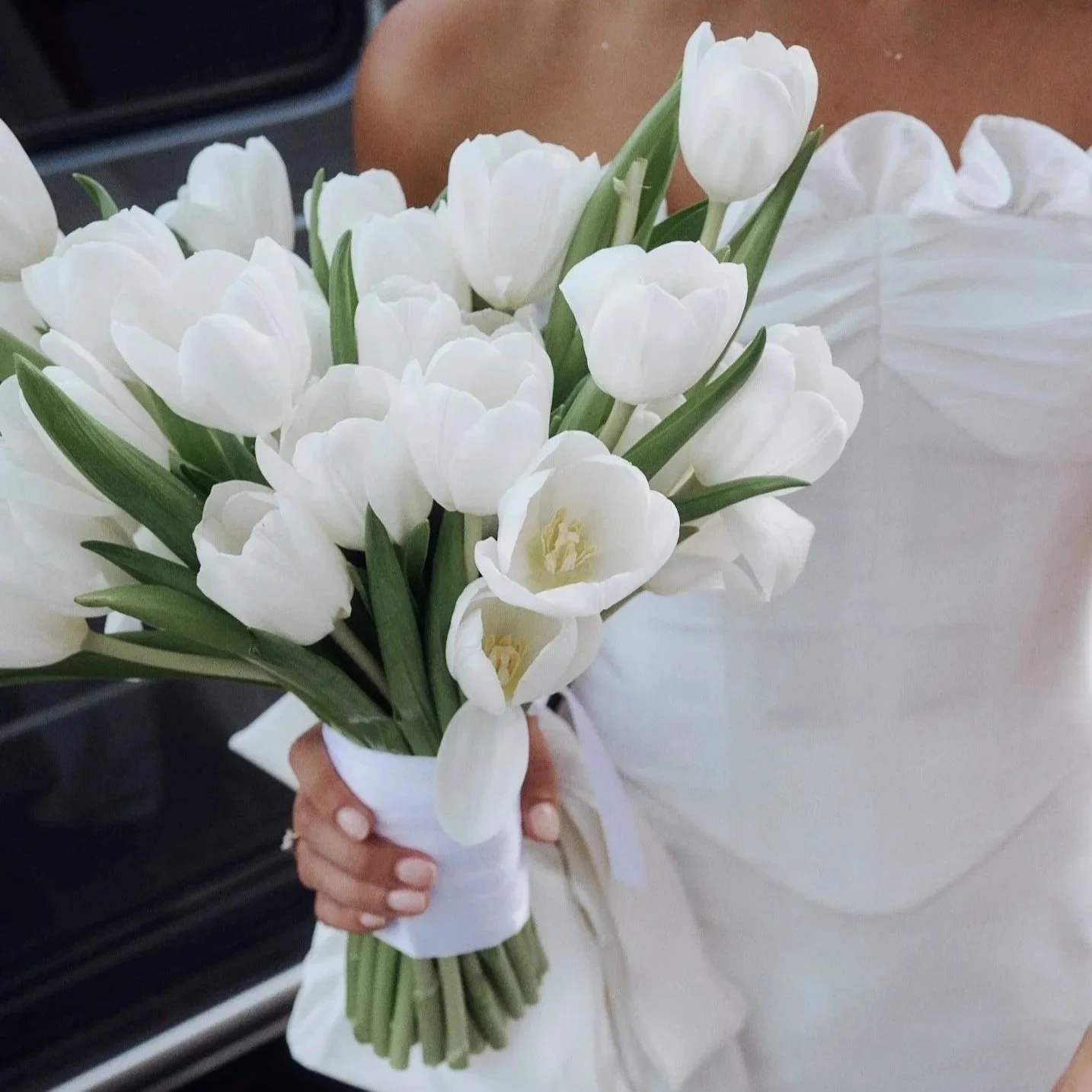 A person holding a bouquet of white tulips wrapped in white ribbon.