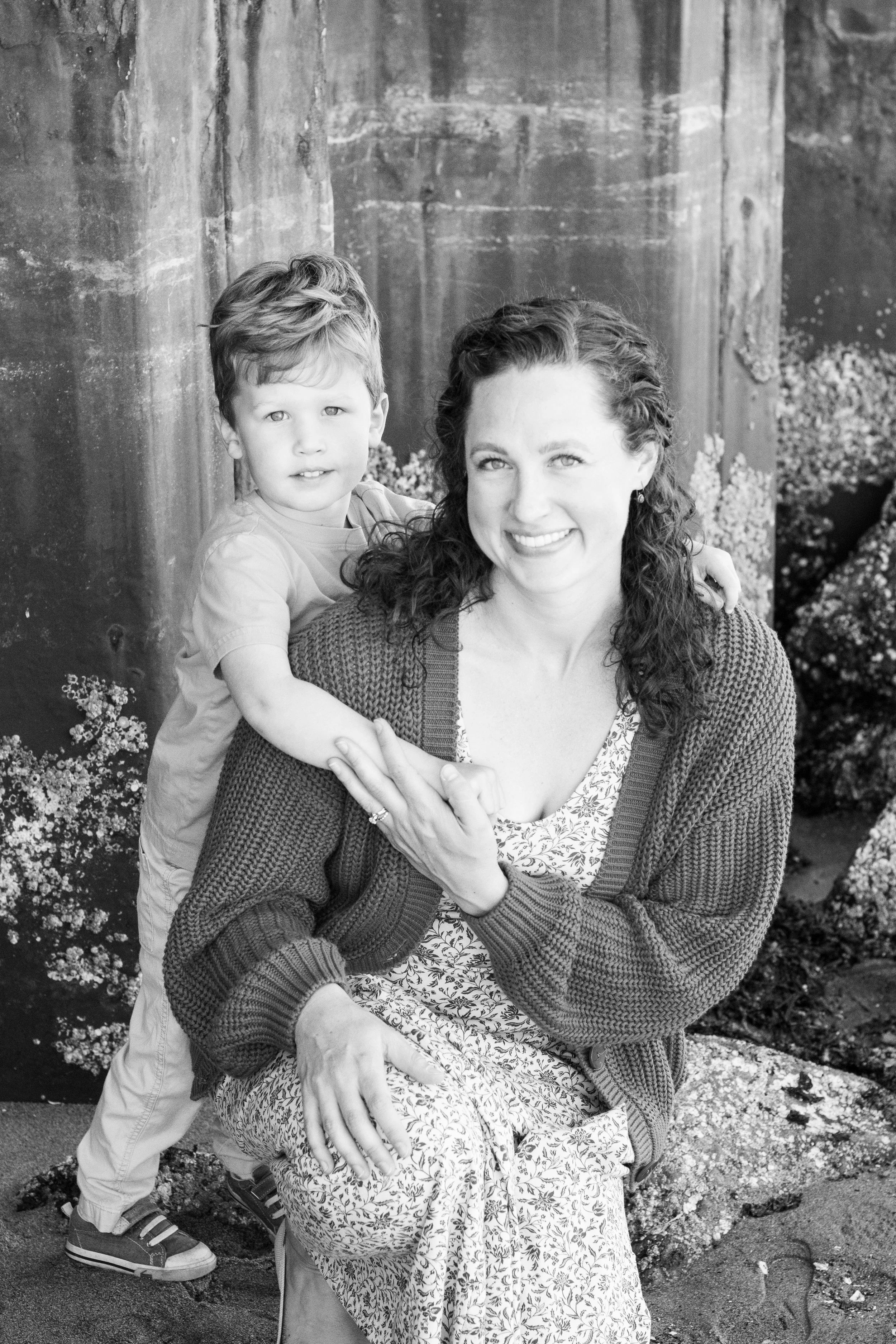 A woman and a young boy outdoors, with the boy sitting on her lap and both smiling.