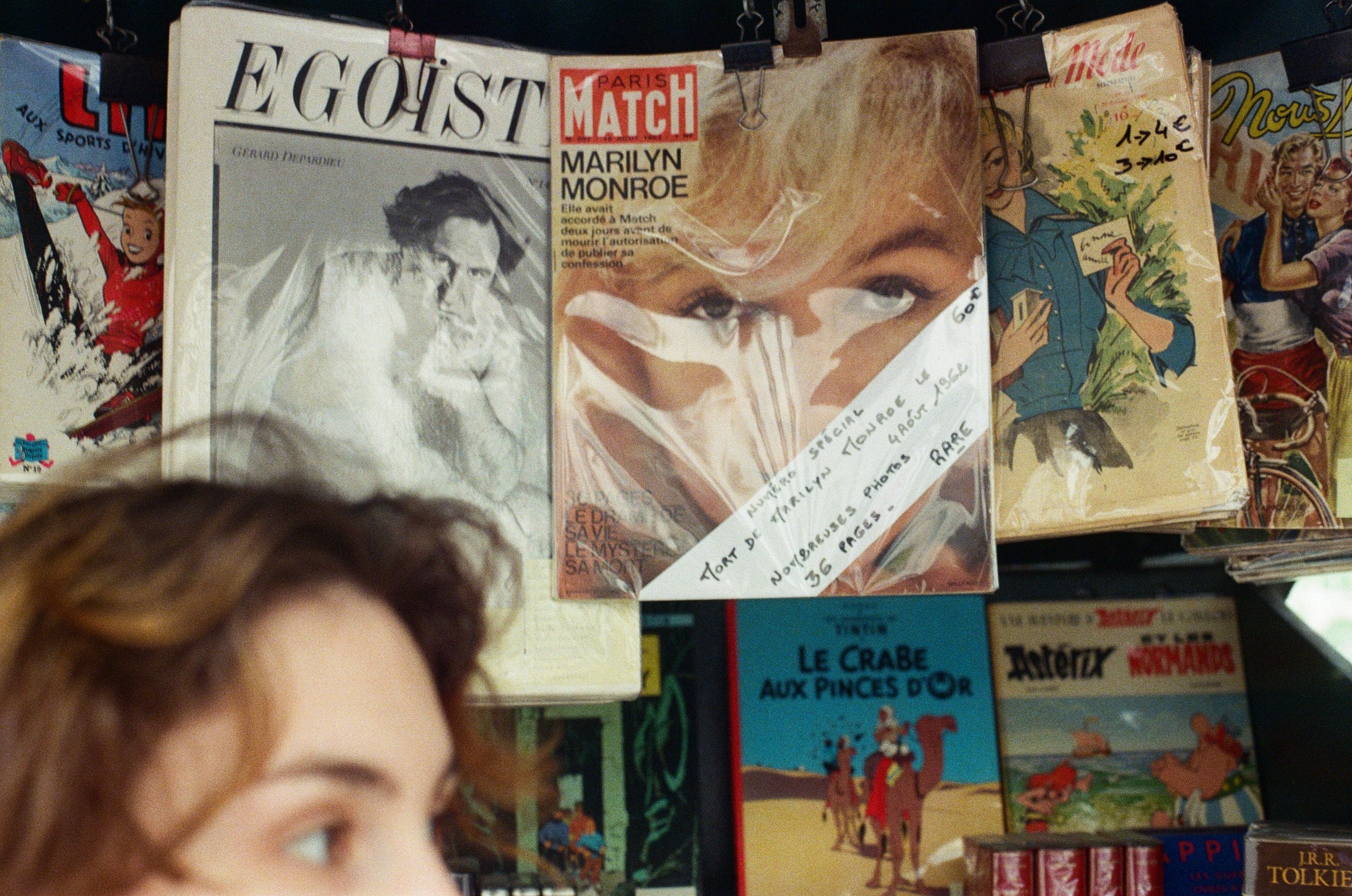 A magazine stand displaying vintage magazines, including a special edition of Paris Match with a cover about Marilyn Monroe, surrounded by other illustrated magazines.