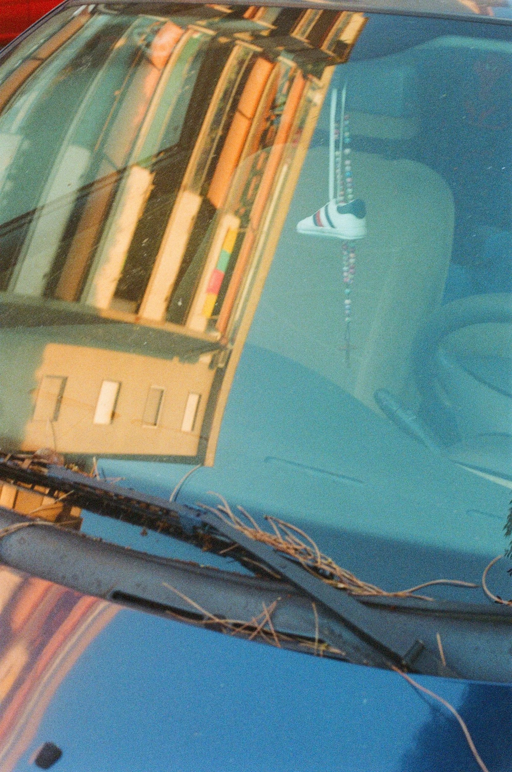 A car's windshield reflecting a building with a covered balcony and a string of lights or decorations hanging in the distance.