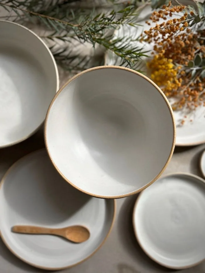 Empty white ceramic bowls, one with a small wooden spoon inside, surrounded by dried flowers and greenery.