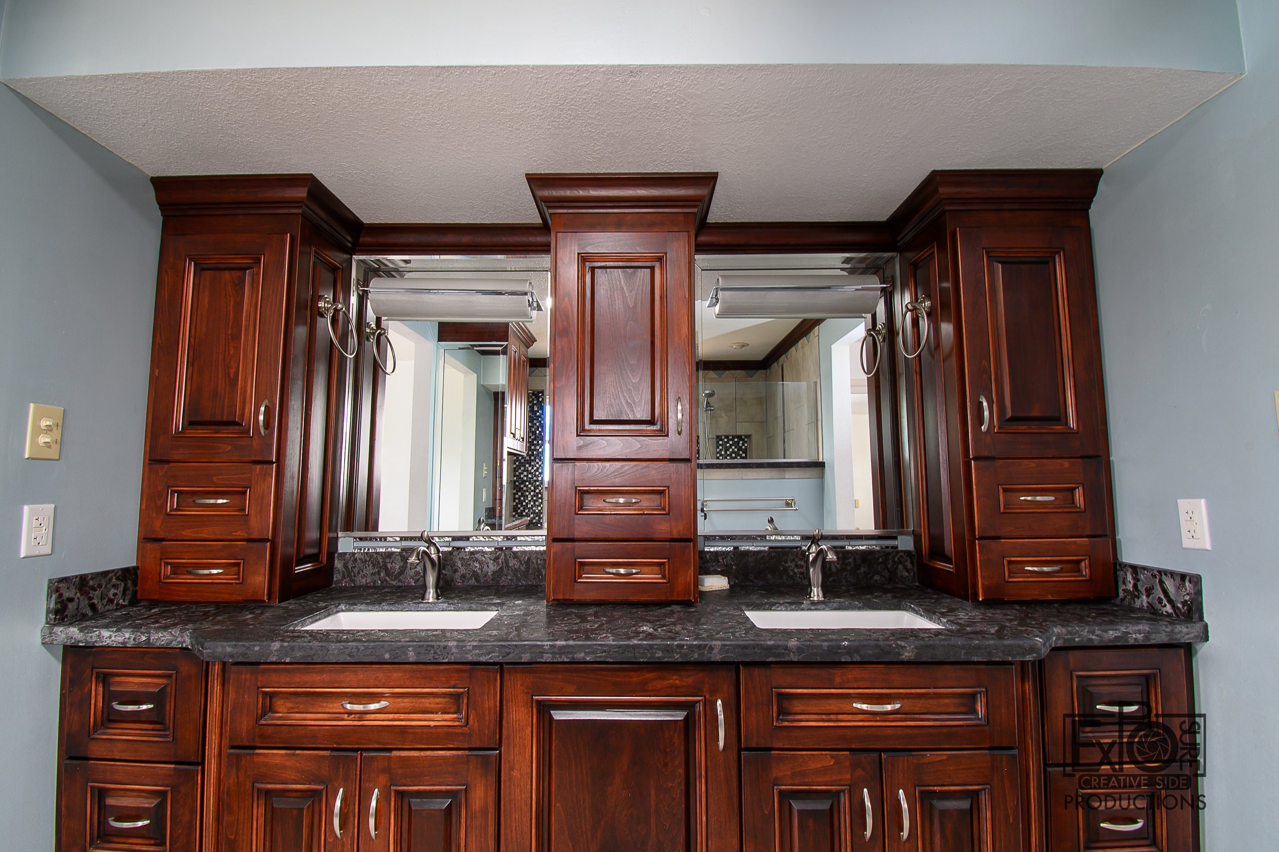 Double bathroom vanity with dark wood cabinets, granite countertops, two sinks, and large mirrors above each sink.