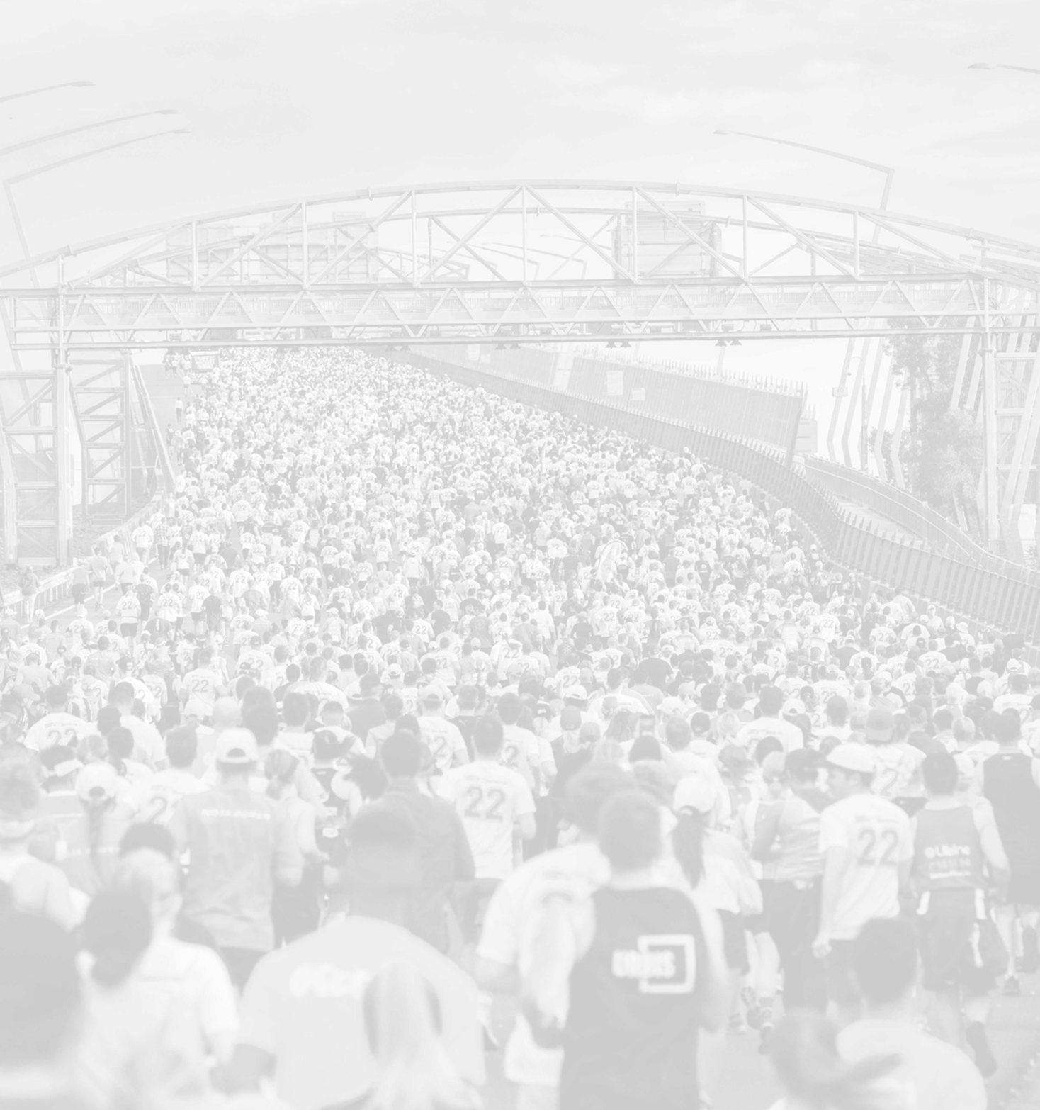 A large crowd of people participating in a marathon or race on a city street, with many wearing numbered bibs and dressed in athletic clothing.