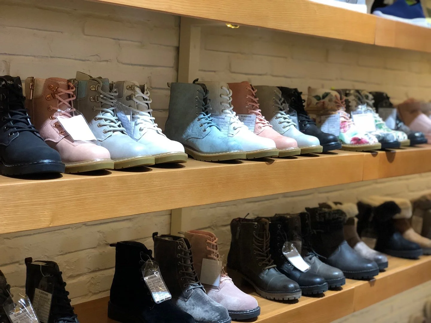 Rows of new fashionable ankle boots in various colors and patterns displayed on wooden shelves in a retail store.