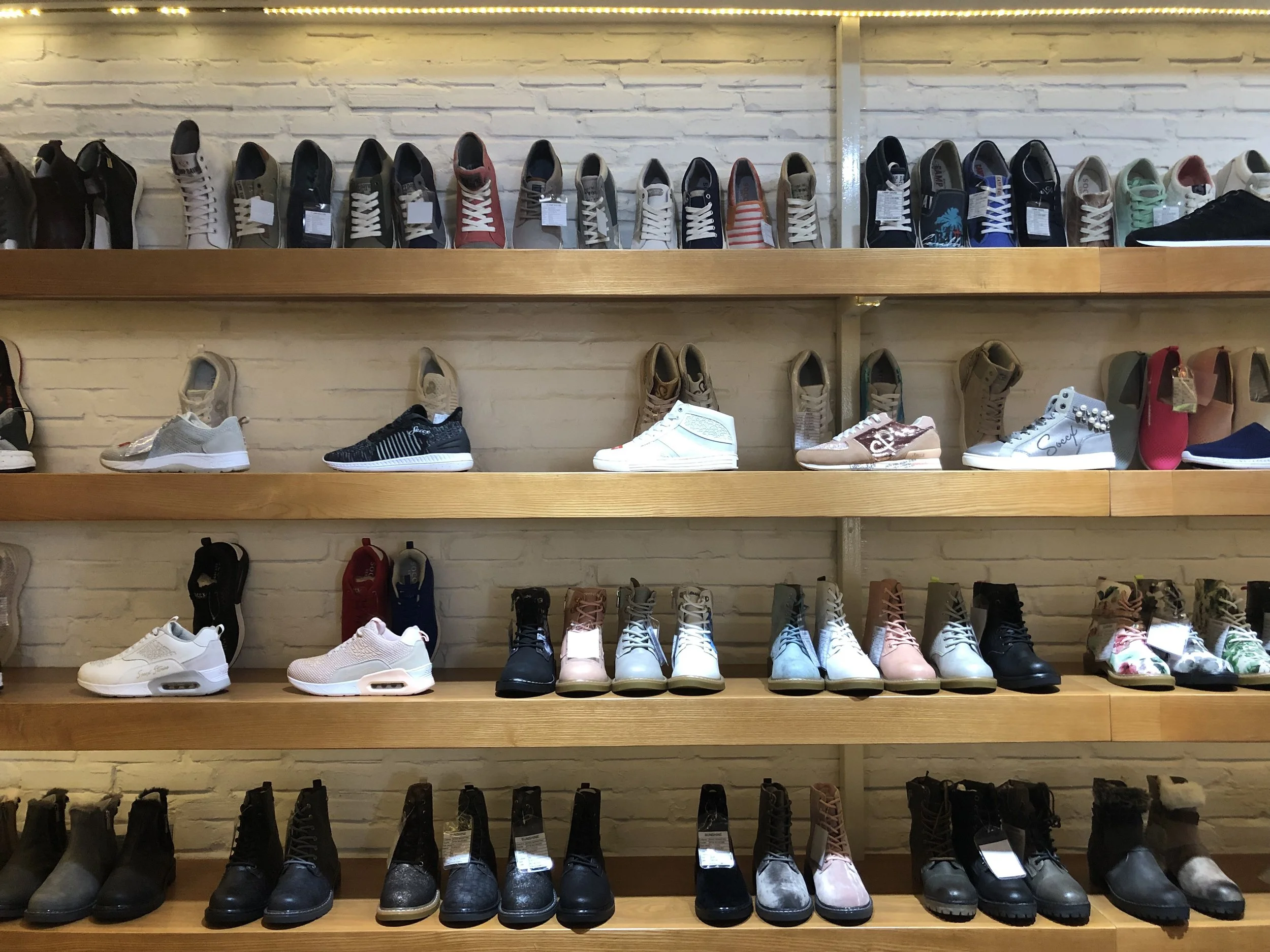 Store display with multiple pairs of sneakers and boots arranged on wooden shelves against a white brick wall.