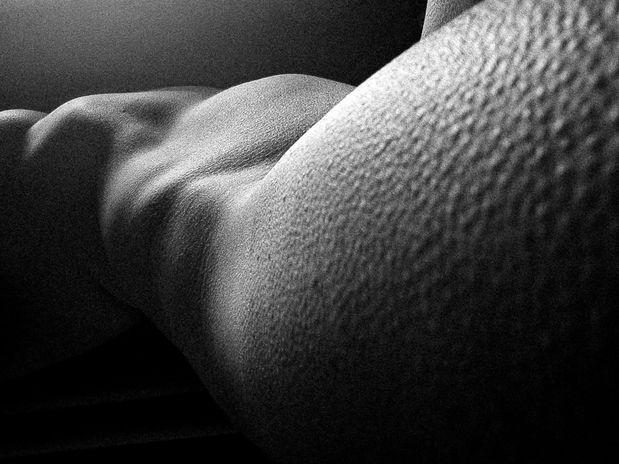 Close-up black and white photo of a person's arm resting on a surface, showing detailed skin texture.