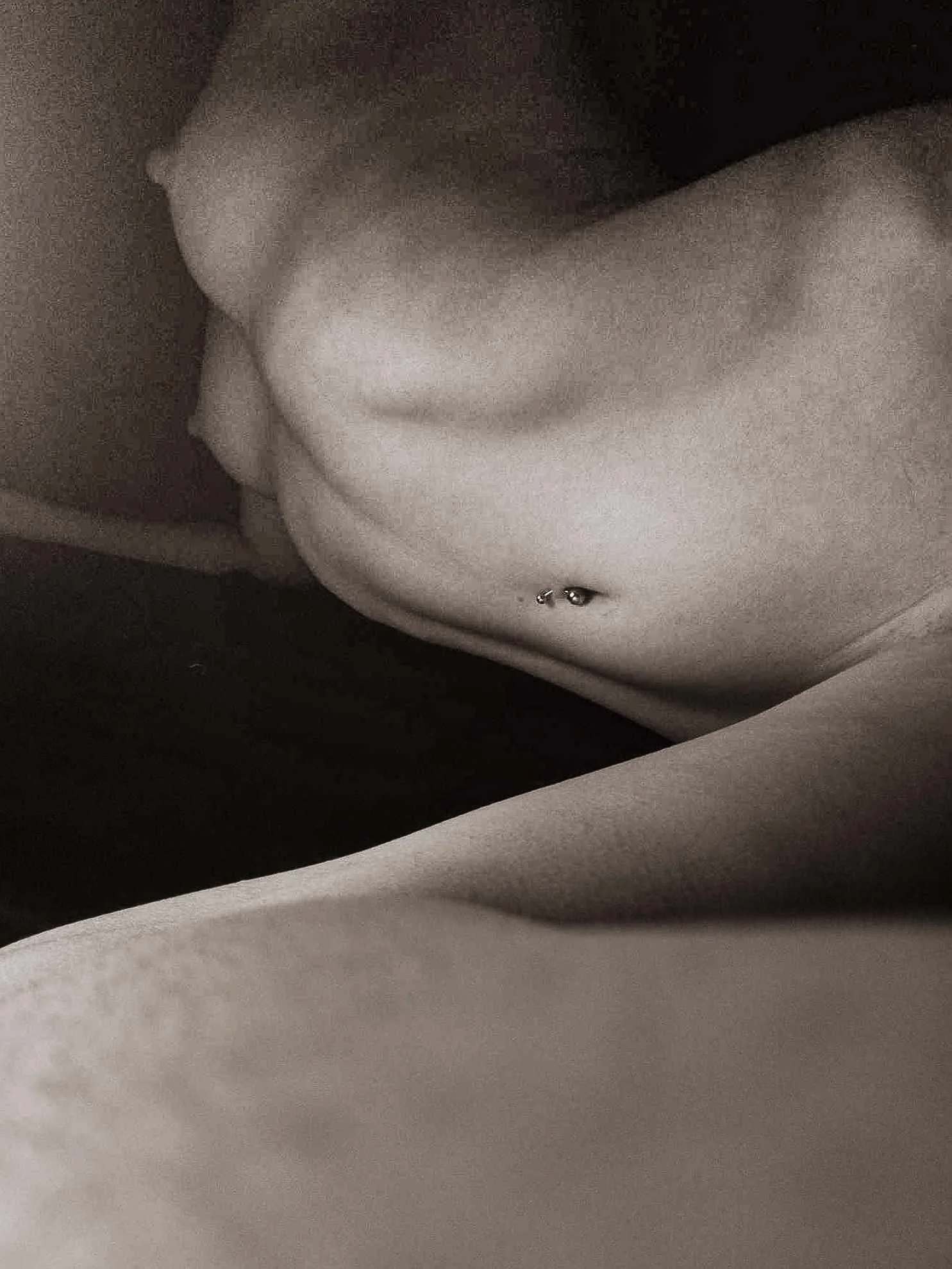 A close-up of a person's bare torso with a navel piercing, lying in a relaxed position.