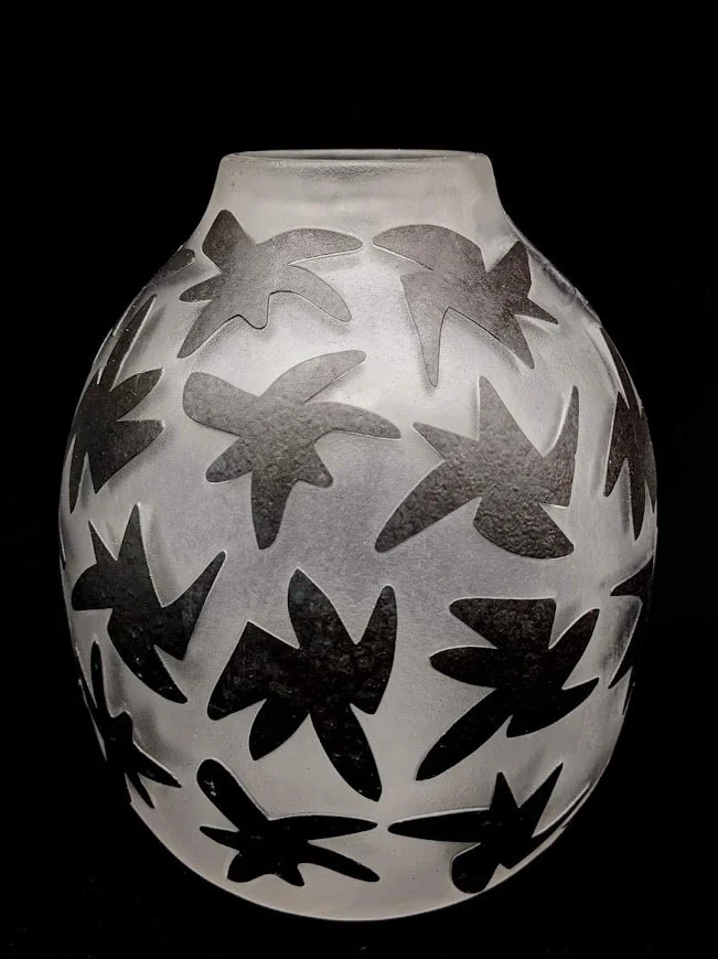 A sand carved frosted glass vase with black icons cutout against a black background.