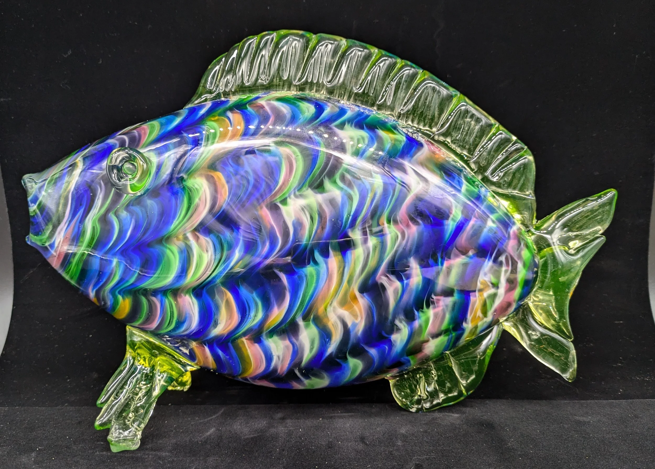 Uranium glass colorful glass fish sculpture with swirled blue, green, yellow, and pink patterns against a black background.