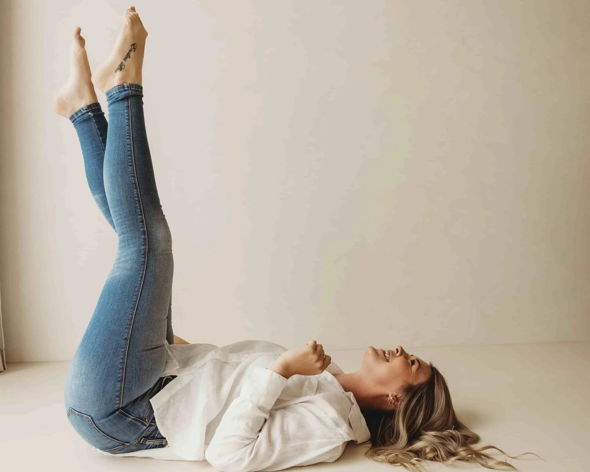 Kiara Jade Trotter lying on her back on the floor with her legs raised vertically laughing and being the best version of herself in a well-lit room with a neutral background.