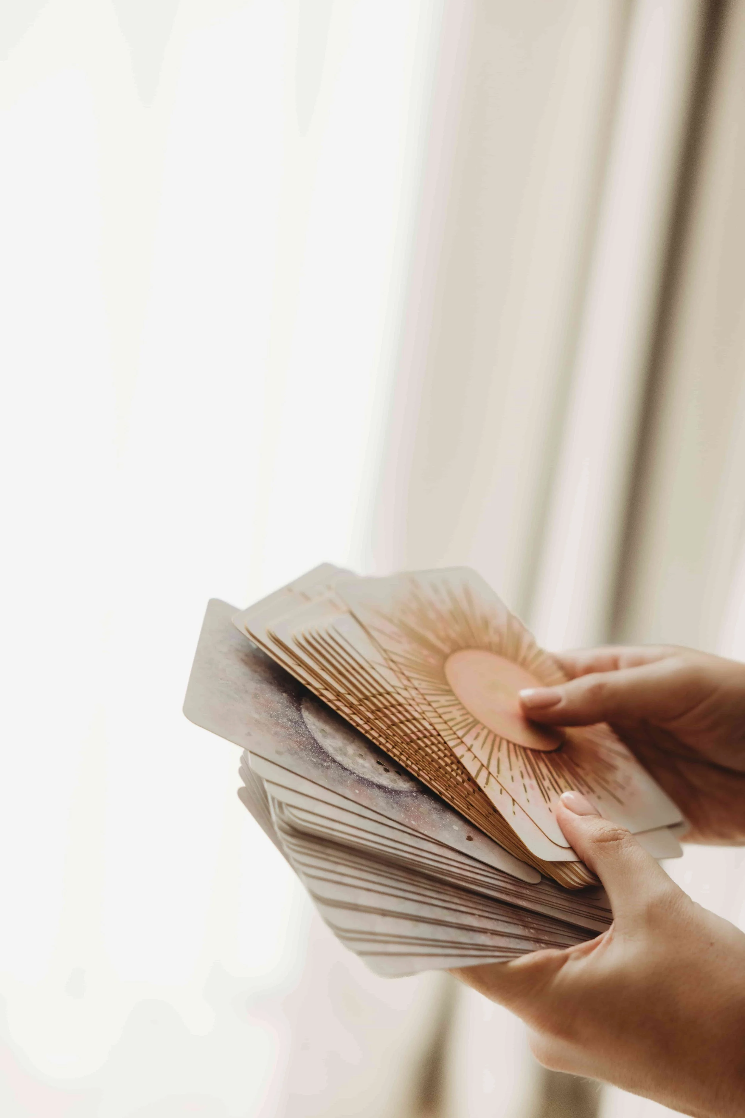 A person's hand holding a fan of energy reading cards, with a background of a light-coloured curtain.