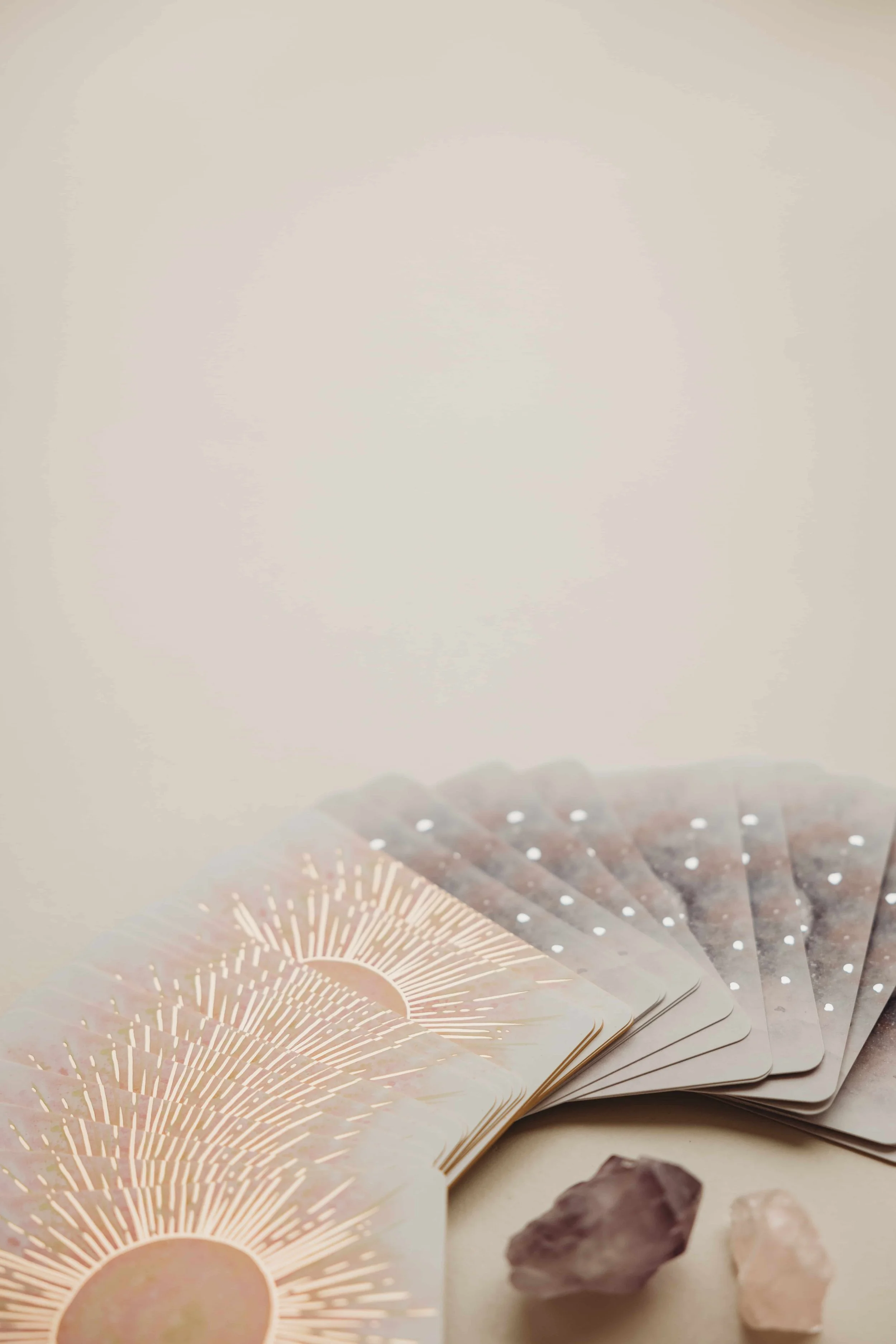 A deck of oracle cards with a radiant sun design, a purple crystal, and a light pink crystal on a light surface.