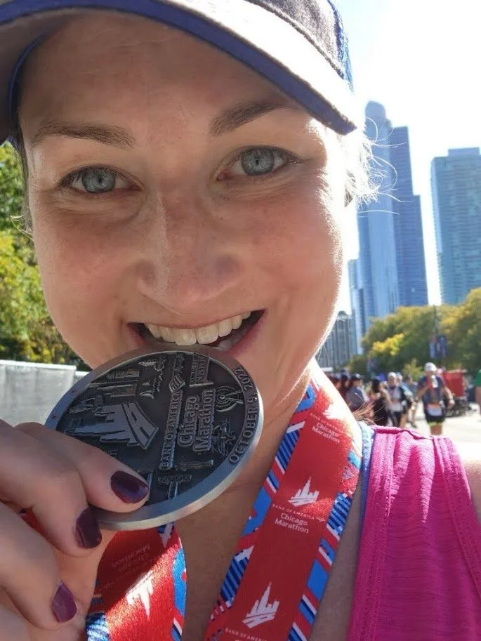 Megan biting her Chicago Marathon finisher medal, with the Chicago skyline behind her