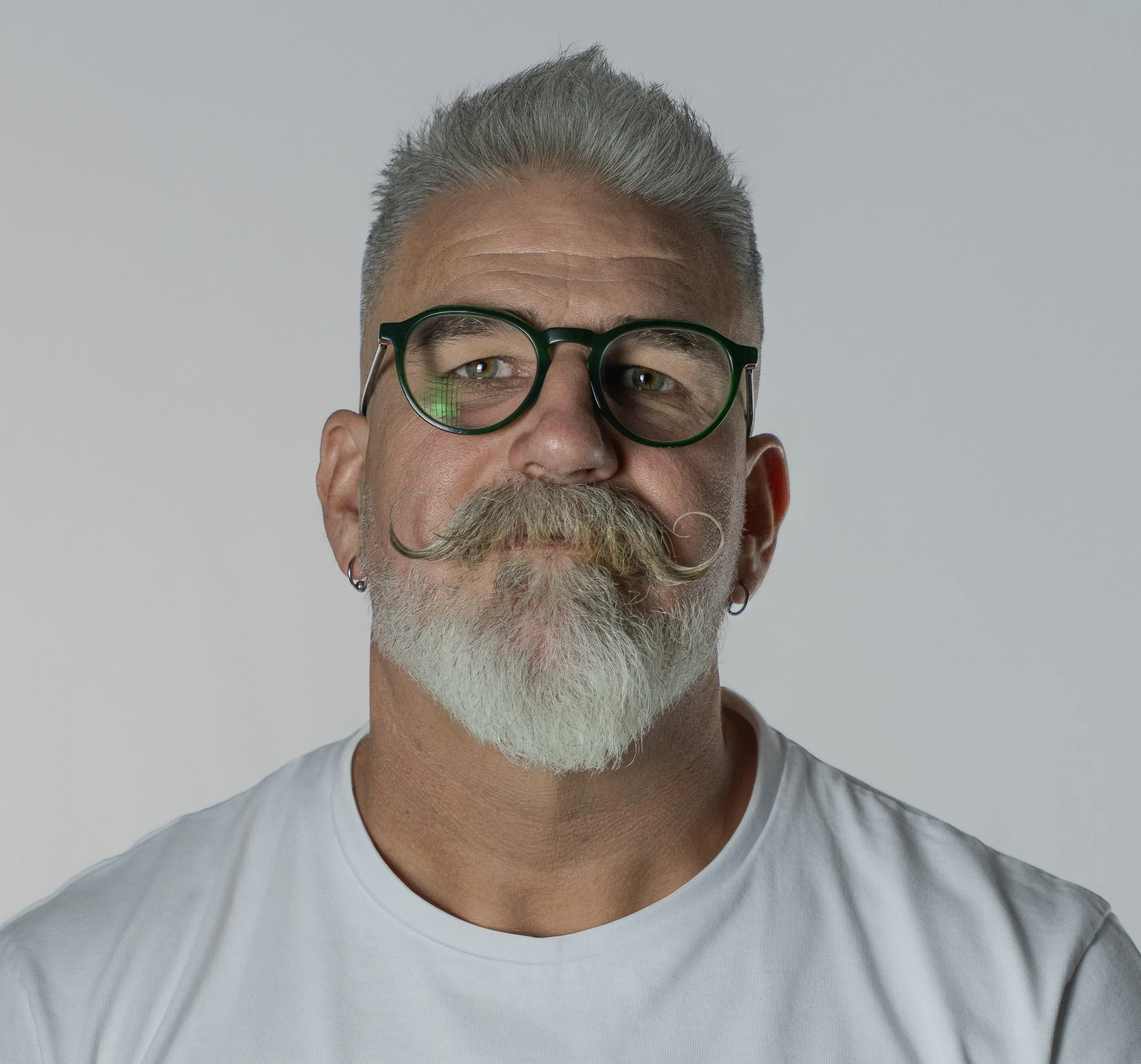 Portrait shot of Dr Christopher Fox - psychosexual therapist & sexologist.. THis is a head shot of a man in his 50s with grey-white hair, beard and a curling moustache.  He wears green-framed glasses.