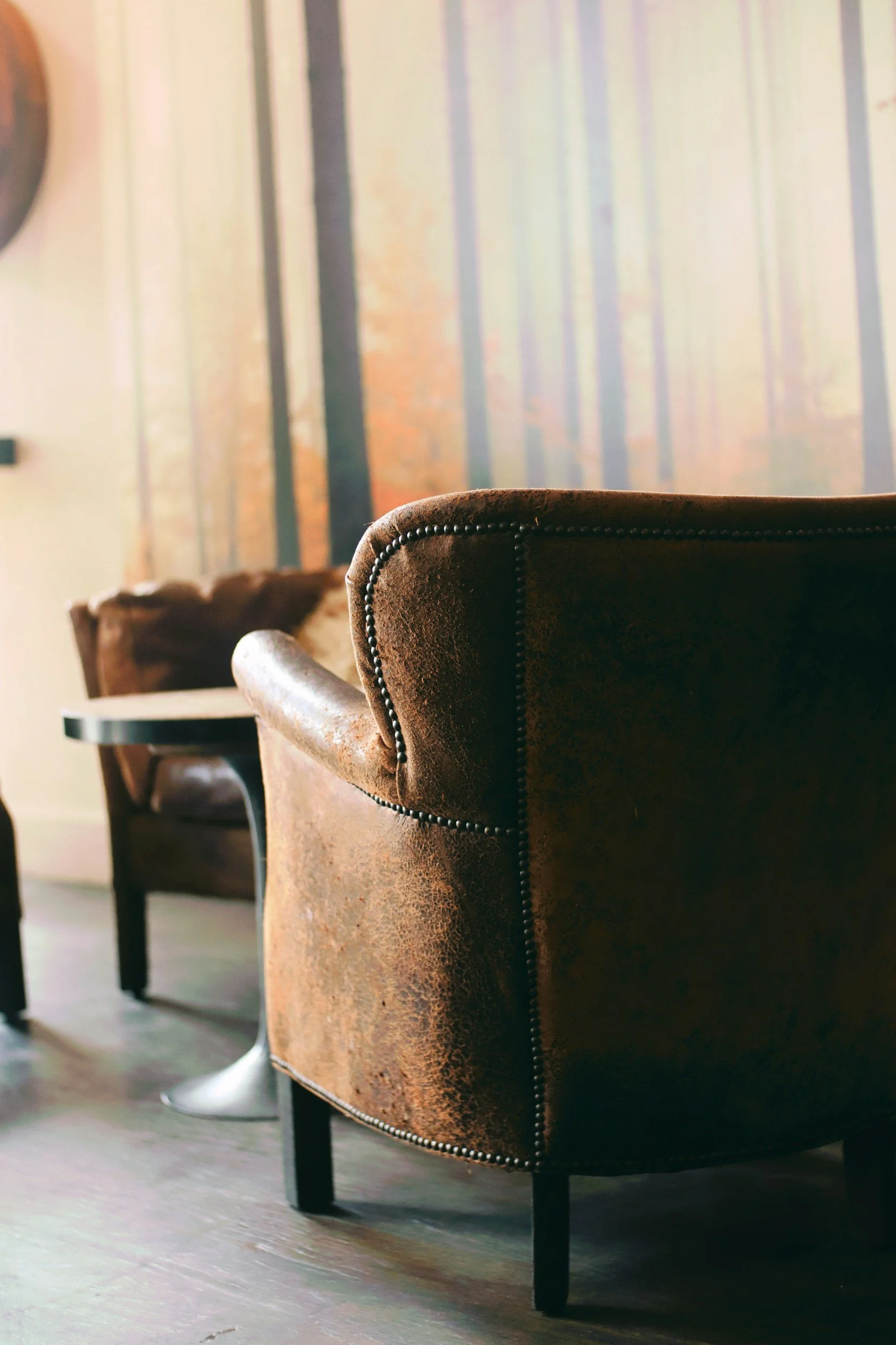 Blick auf eine braune Ledercouch in einem Wohnzimmer, im Hintergrund durch Fenster sichtbare vertikale Vorhänge.