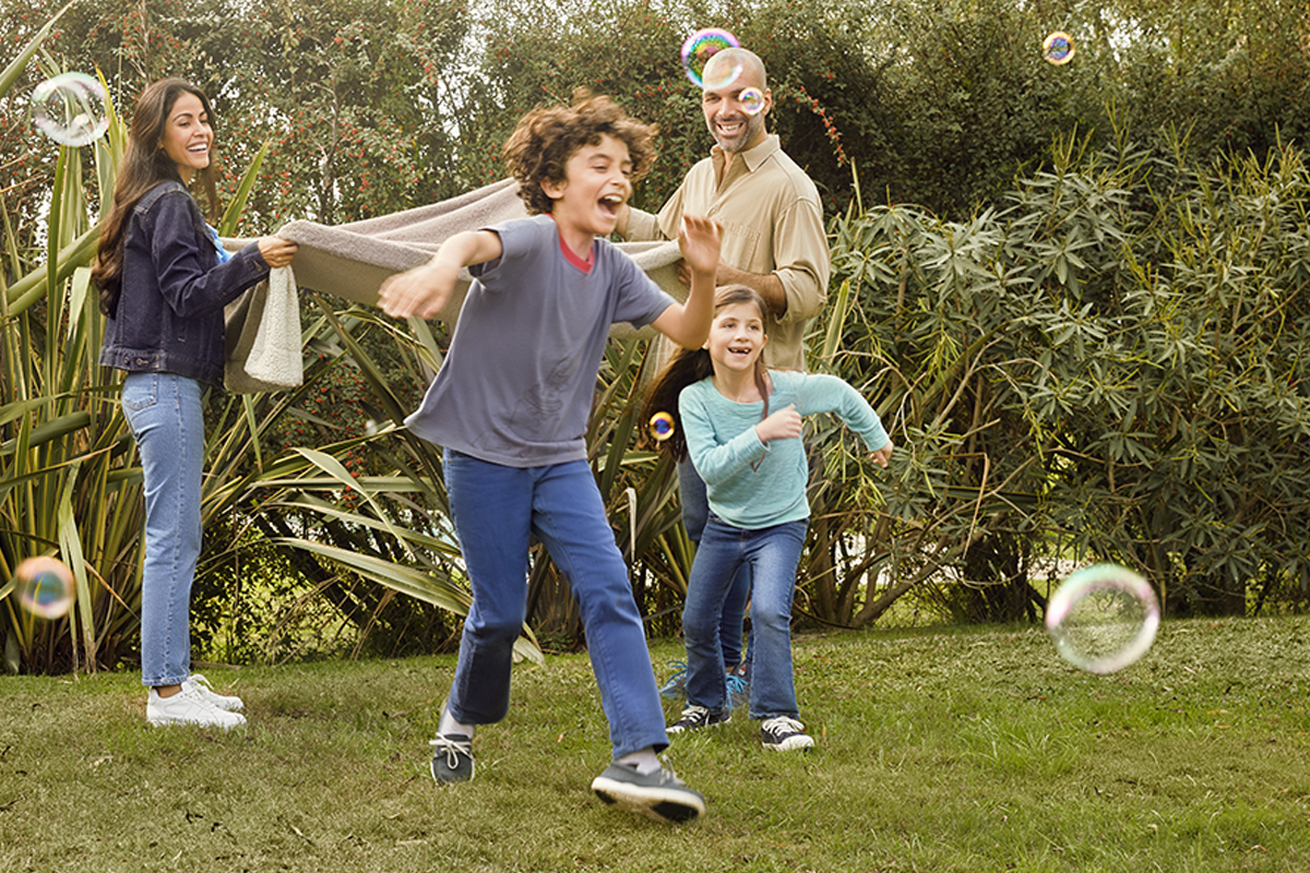 Family playing outdoors with bubbles and a blanket, surrounded by greenery. Captures the lifestyle benefits of U.S. residency through investment immigration programs like the EB5 visa.