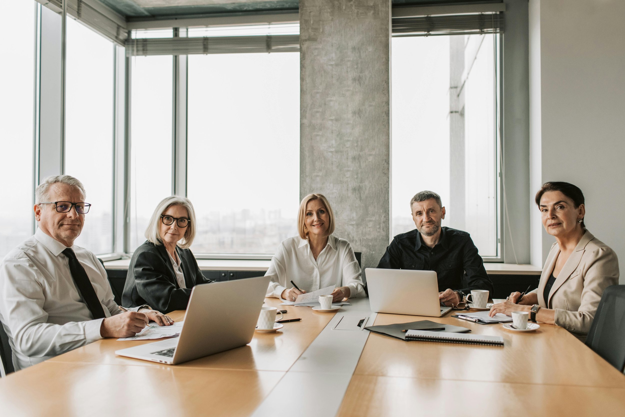 Five business professionals seated around a conference table with laptops and documents. Represents collaborative EB5 investment planning and due diligence for securing U.S. permanent residency.