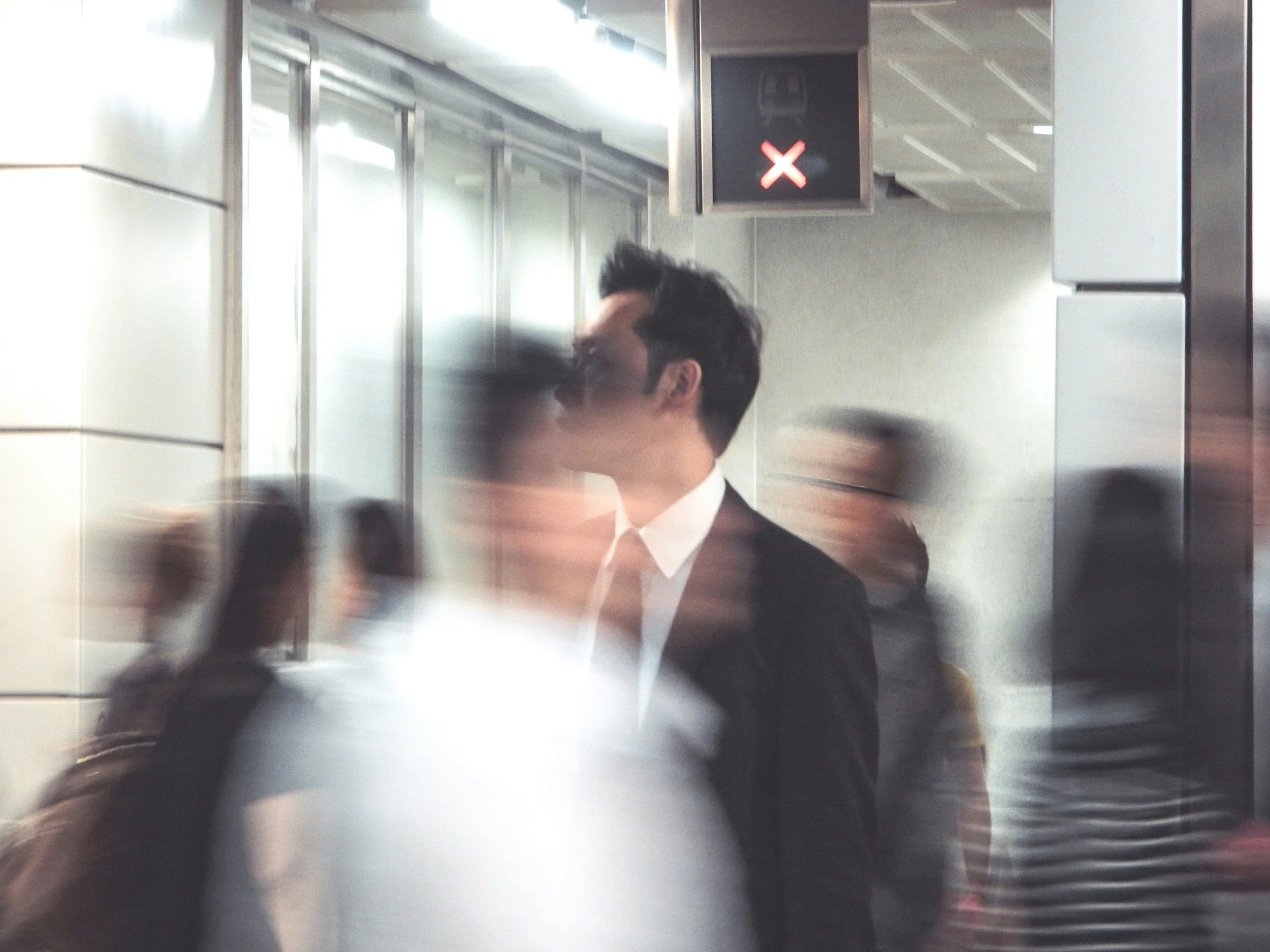 An individual in business attire stands still as commuters rush past in a subway station, representing the pressure of choosing between EB5 and E-2 visa options.