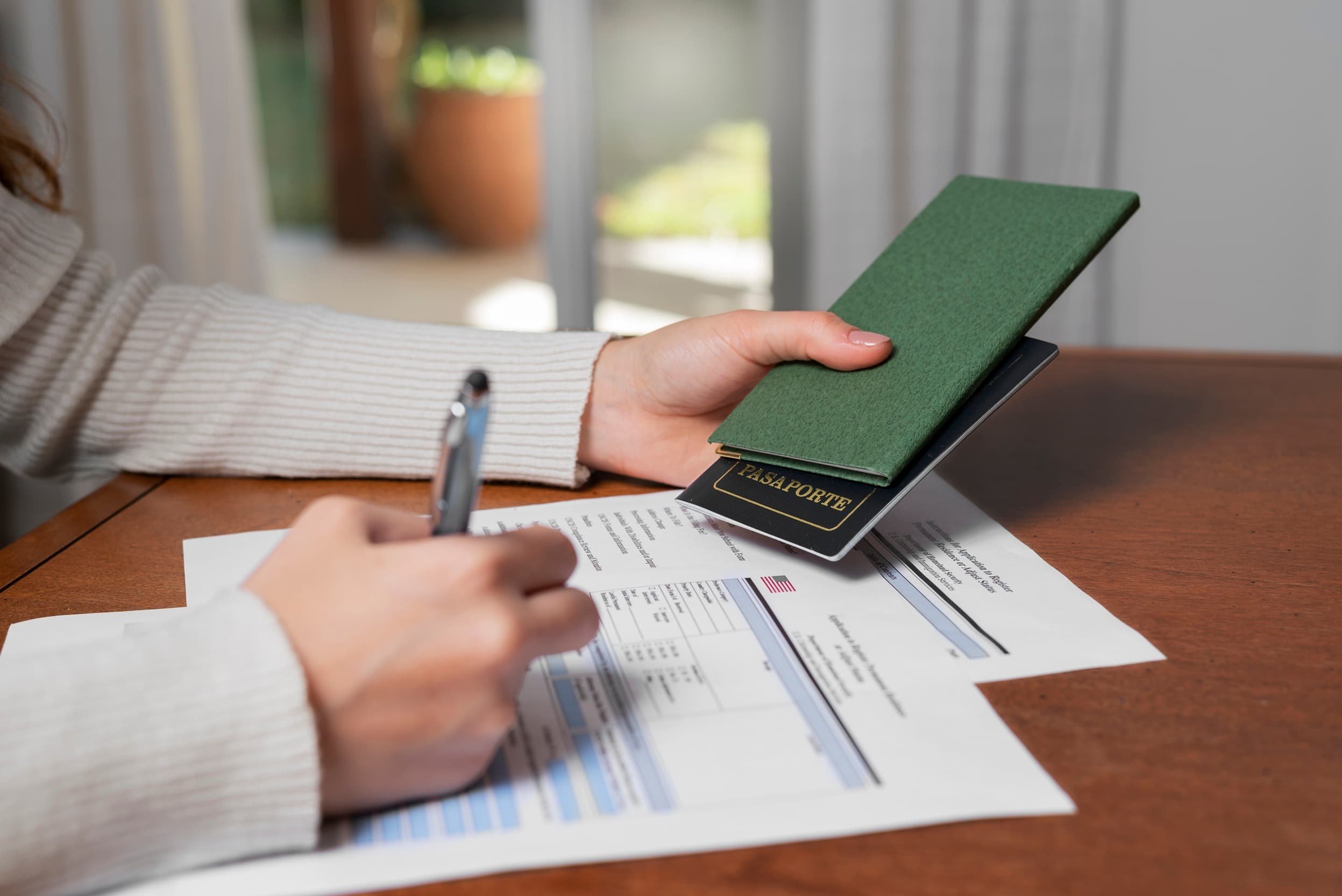 Close-up of a person holding a passport and filling out immigration forms at a wooden desk, symbolizing the EB5 visa application process under the RIA.