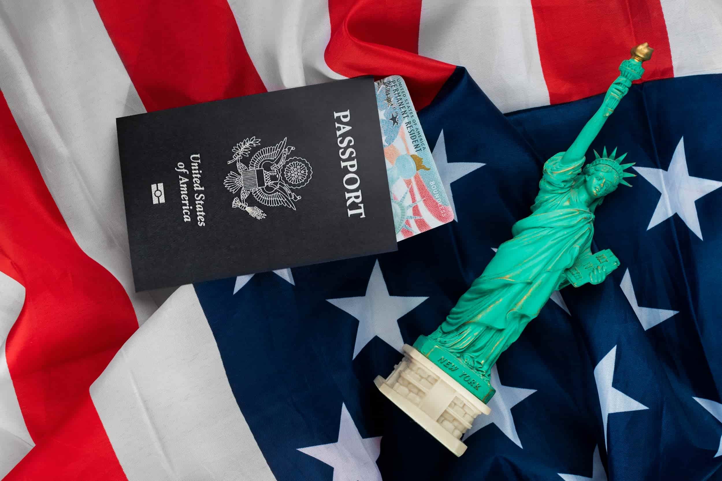 U.S. passport, permanent resident card, and miniature Statue of Liberty placed on an American flag, representing successful EB5 immigration outcomes with the help of Arcasia Advisors.