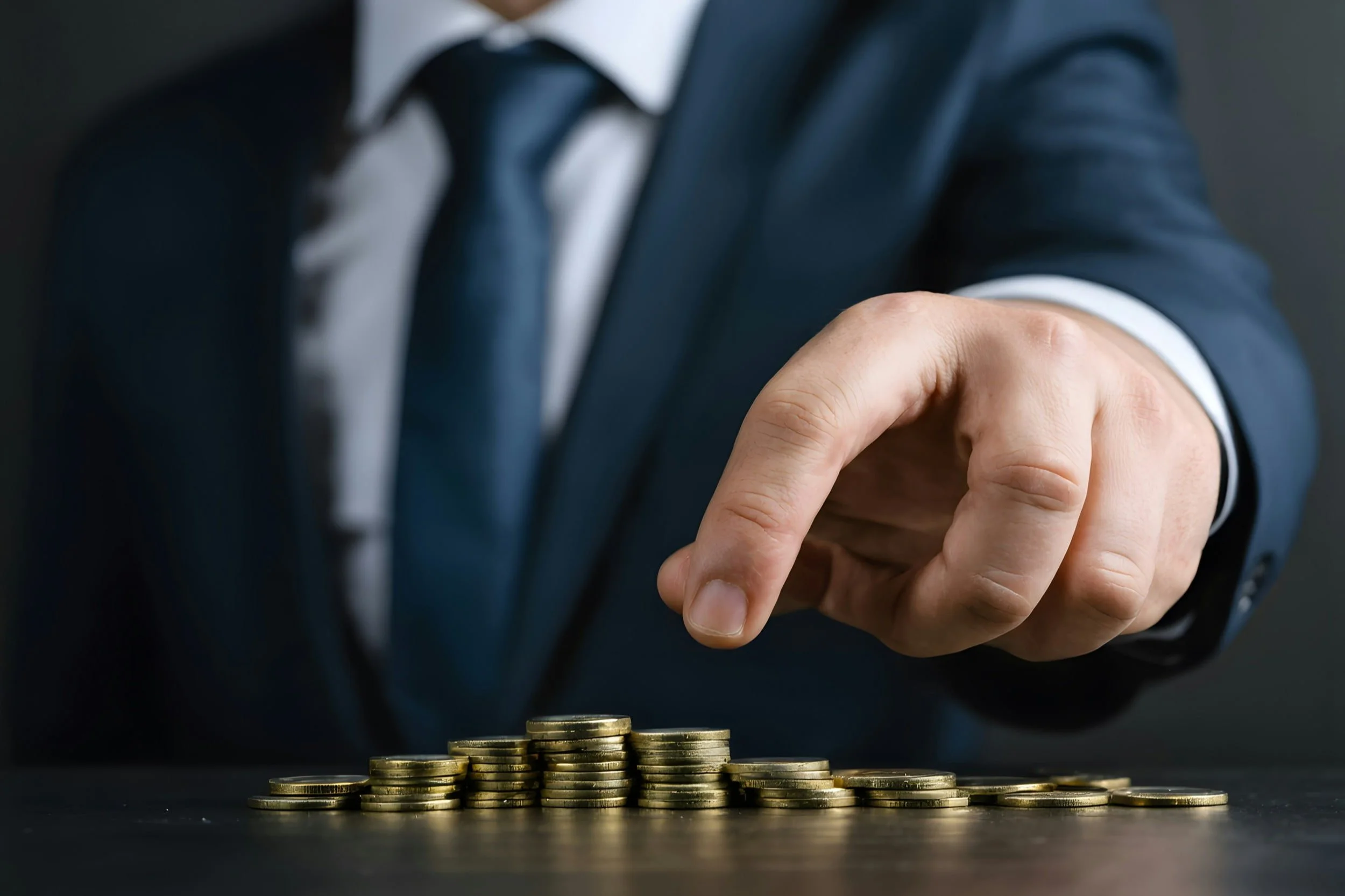 Close-up of a businessman in a suit stacking gold coins, symbolizing EB5 investment decisions and the importance of eb5 agents.
