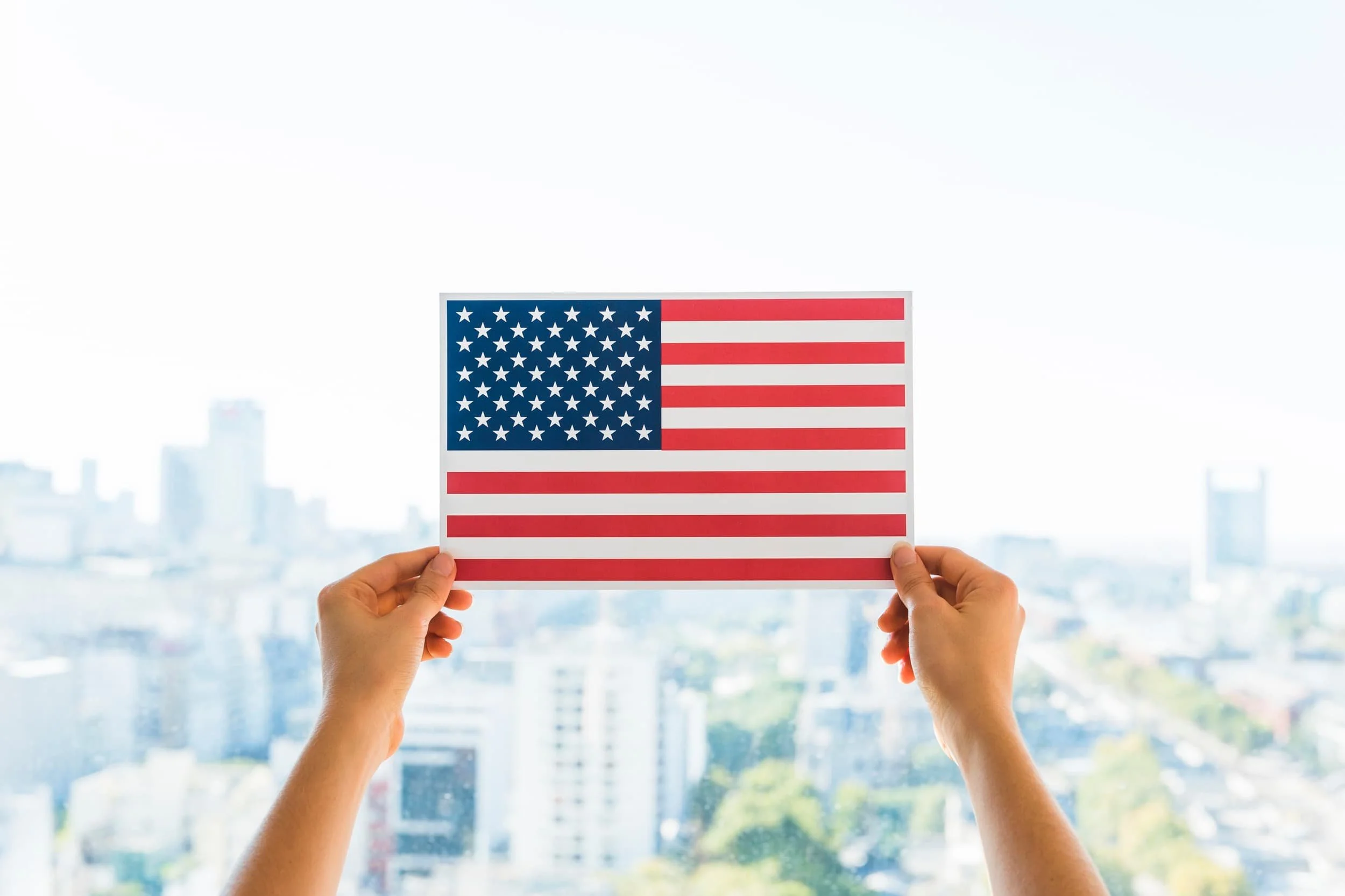 Person holding U.S. flag in front of city skyline, representing EB5 investors choosing between AOS and consular processing for a green card through investment in real estate.