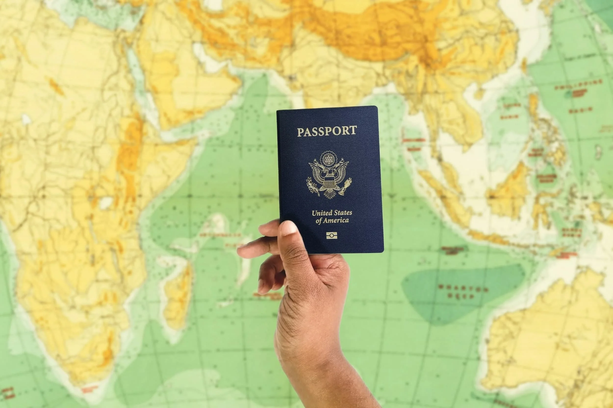 Hand holding a U.S. passport in front of a world map, representing global EB5 investors securing permanent residency and eventual U.S. citizenship before the 2027 deadline.
