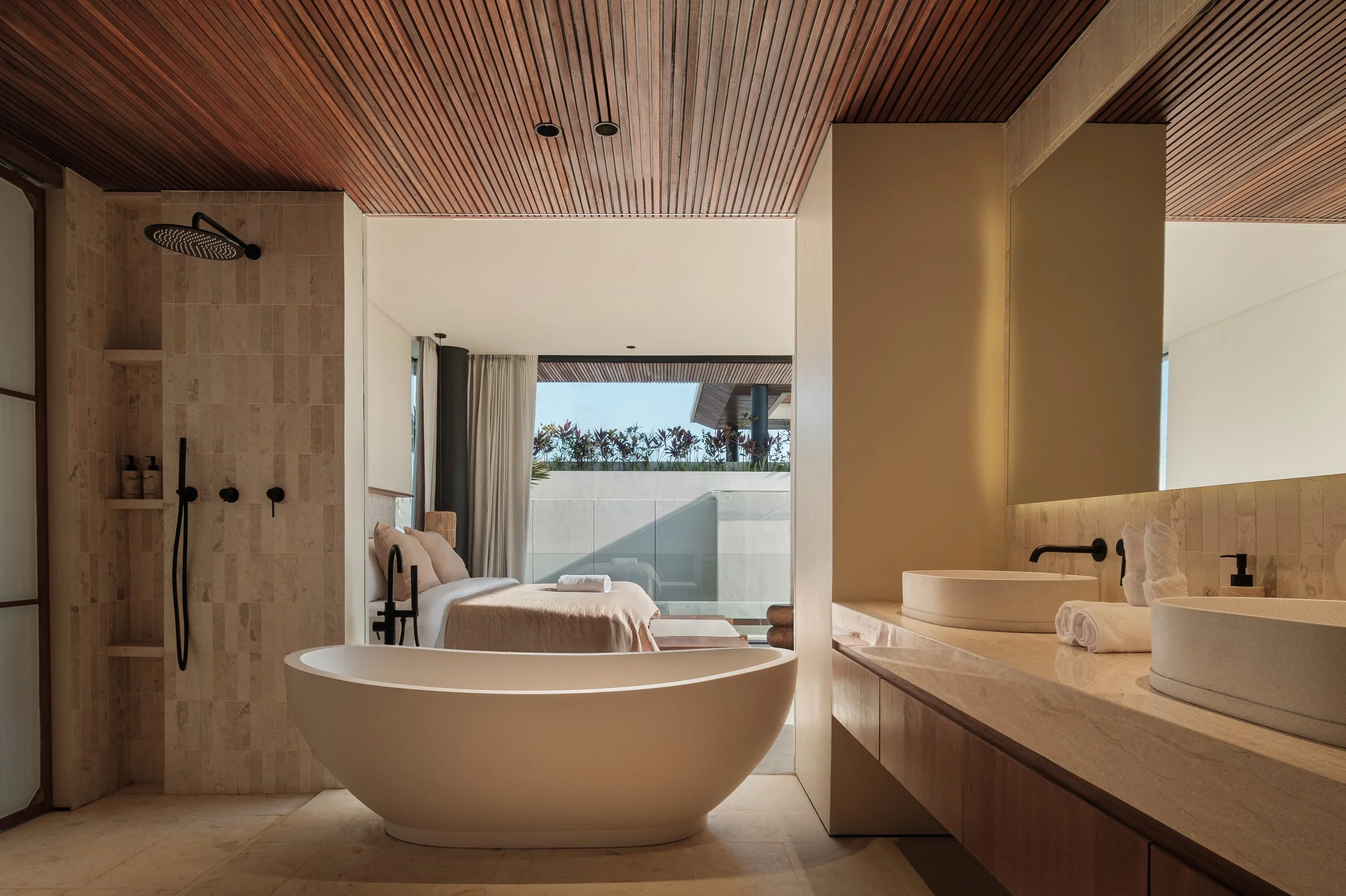 Modern bathroom with a freestanding bathtub, a walk-in shower with a rain showerhead, and a large window overlooking a balcony with plants.