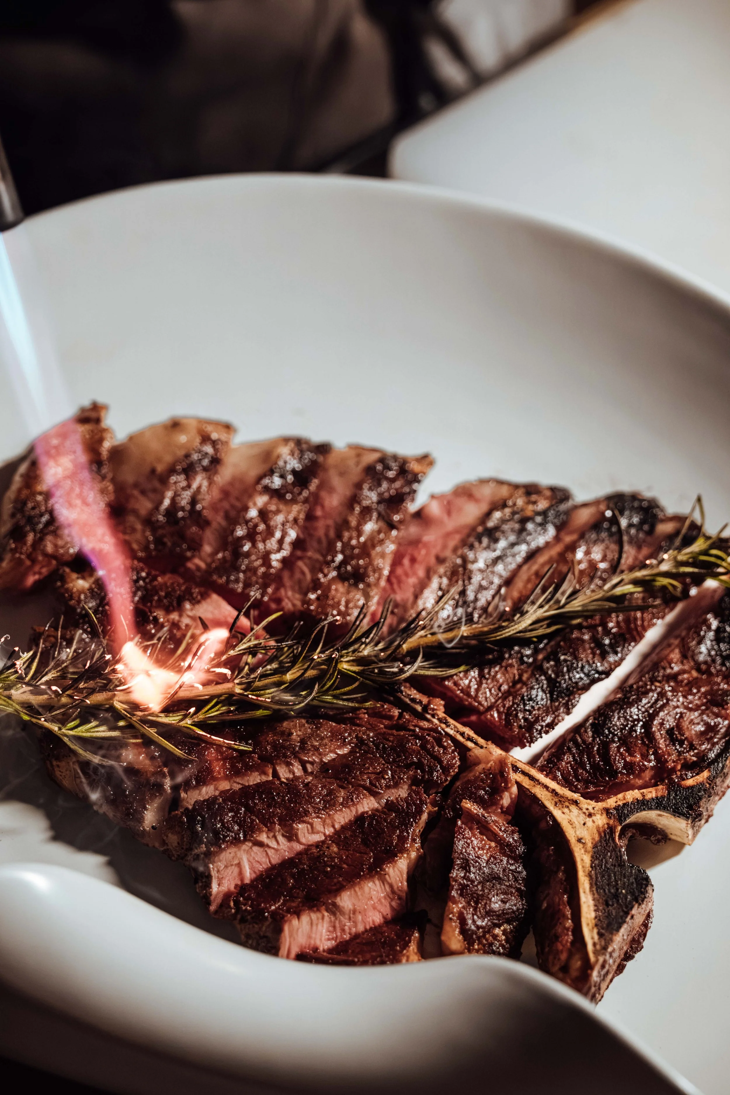 Slices of grilled steak garnished with rosemary on a white serving dish.