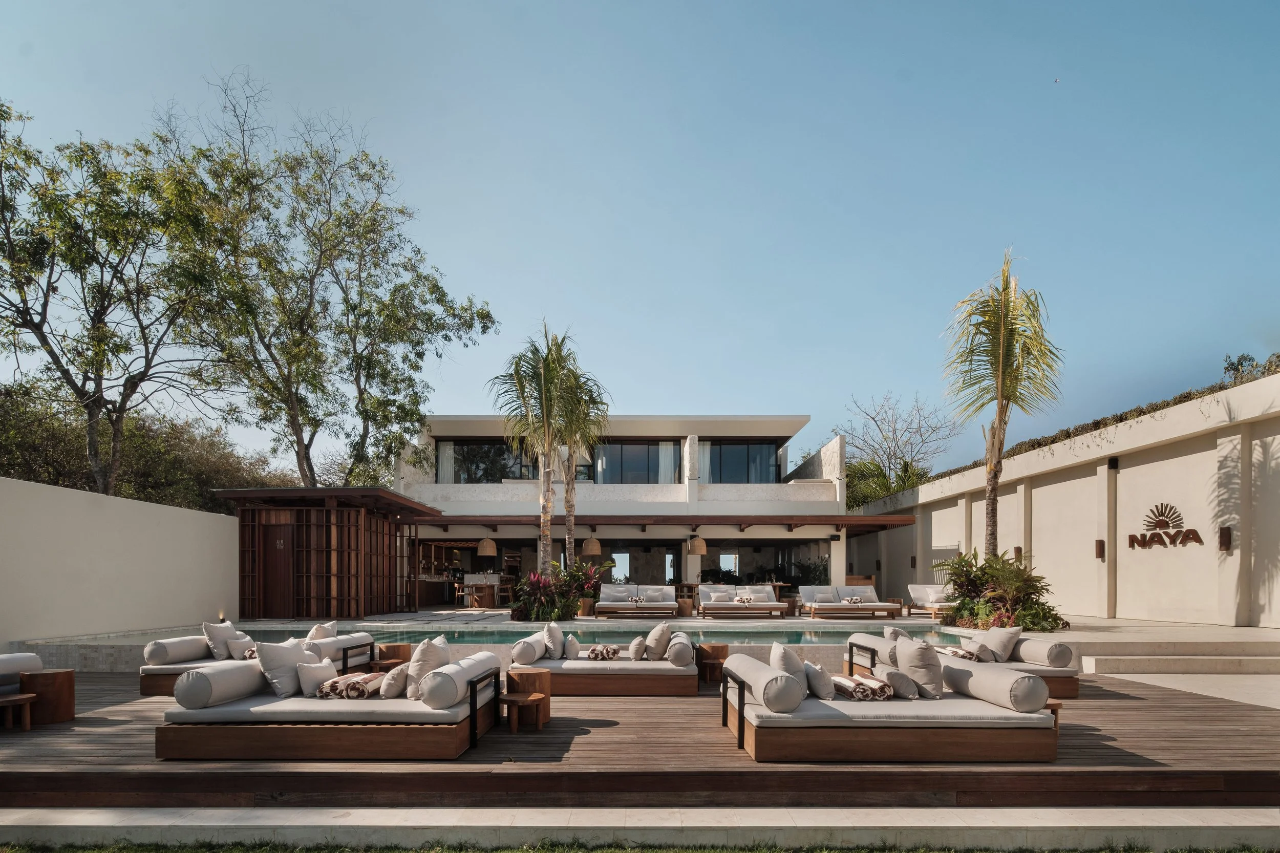 Outdoor lounge area at a modern building with white seating, wooden accents, and palm trees, under a clear blue sky.