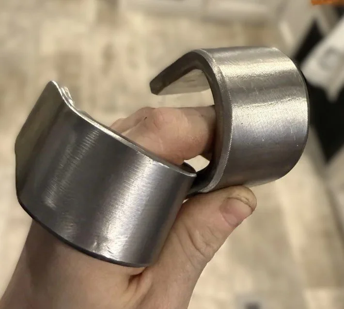 A person holding a metal bearing with a split and a hook on one side.