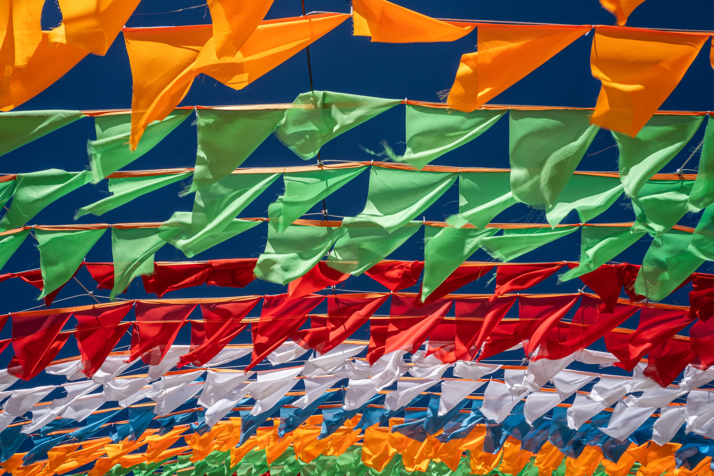 Colorful triangular flags hanging in rows against a blue sky.