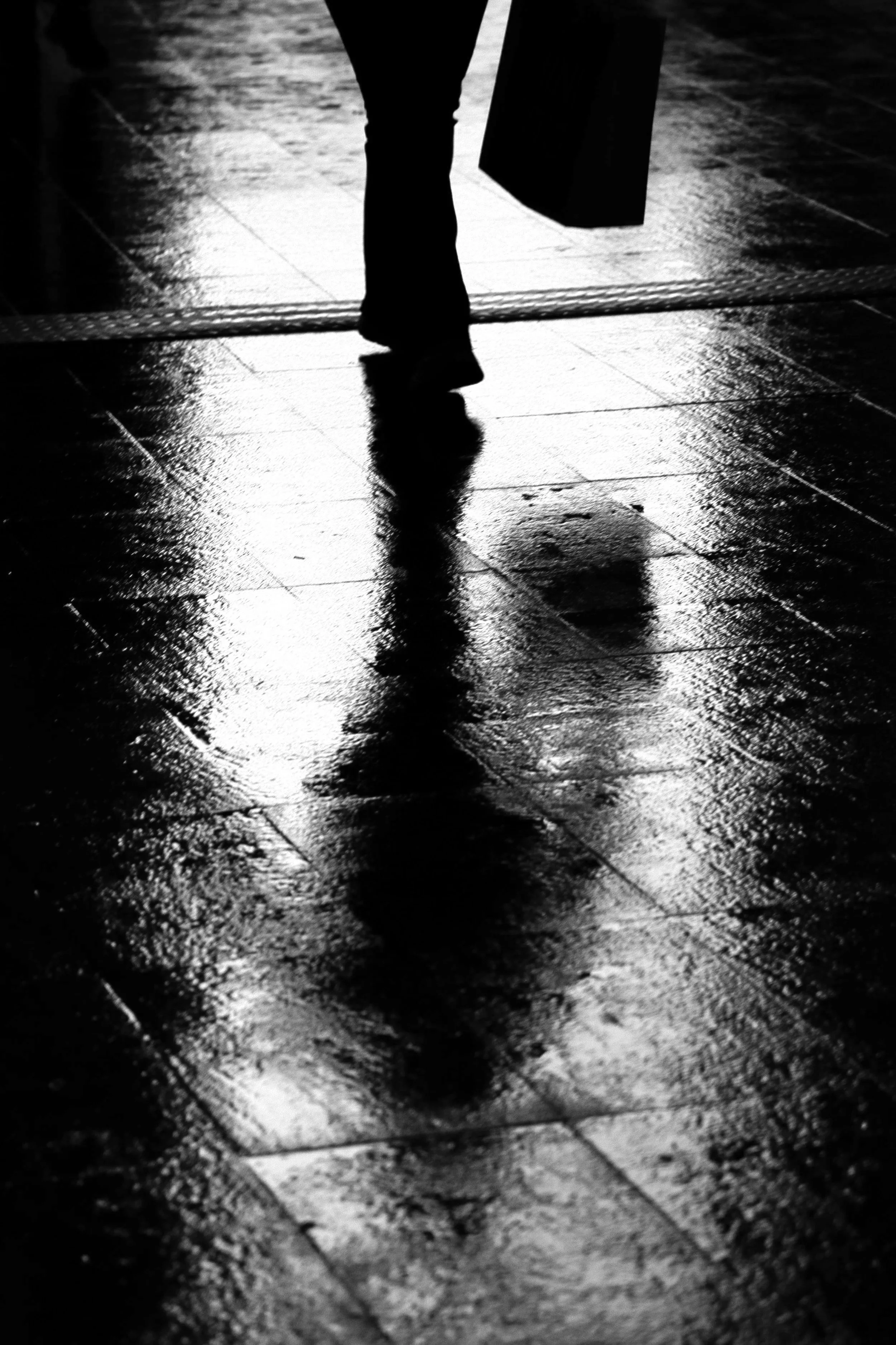 Silhouette of a person walking on wet pavement at night, with purple reflections on the ground.