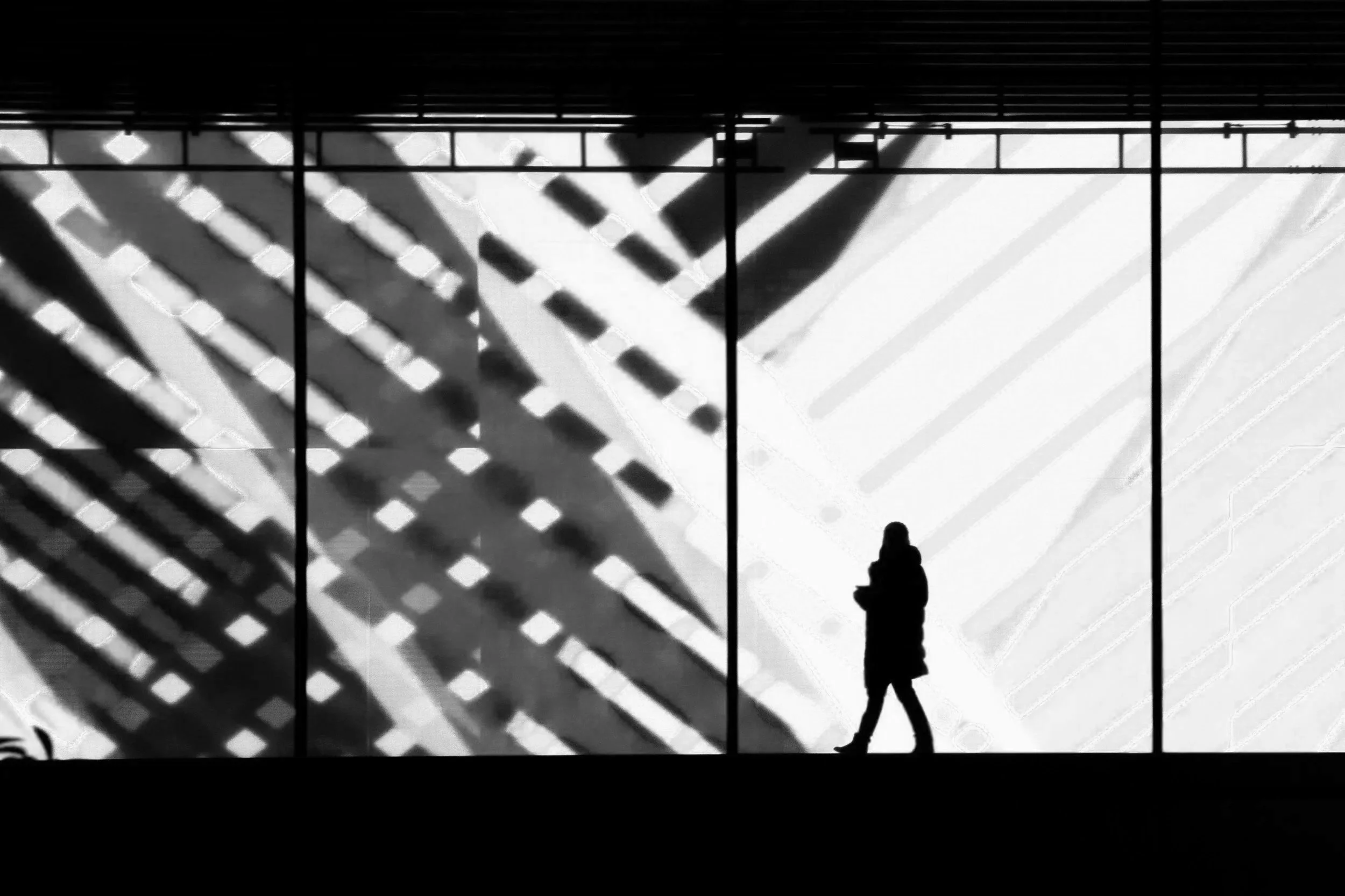 Silhouette of a person walking past a large colorful digital display with diagonal red, blue, yellow, and white lines and patterns.