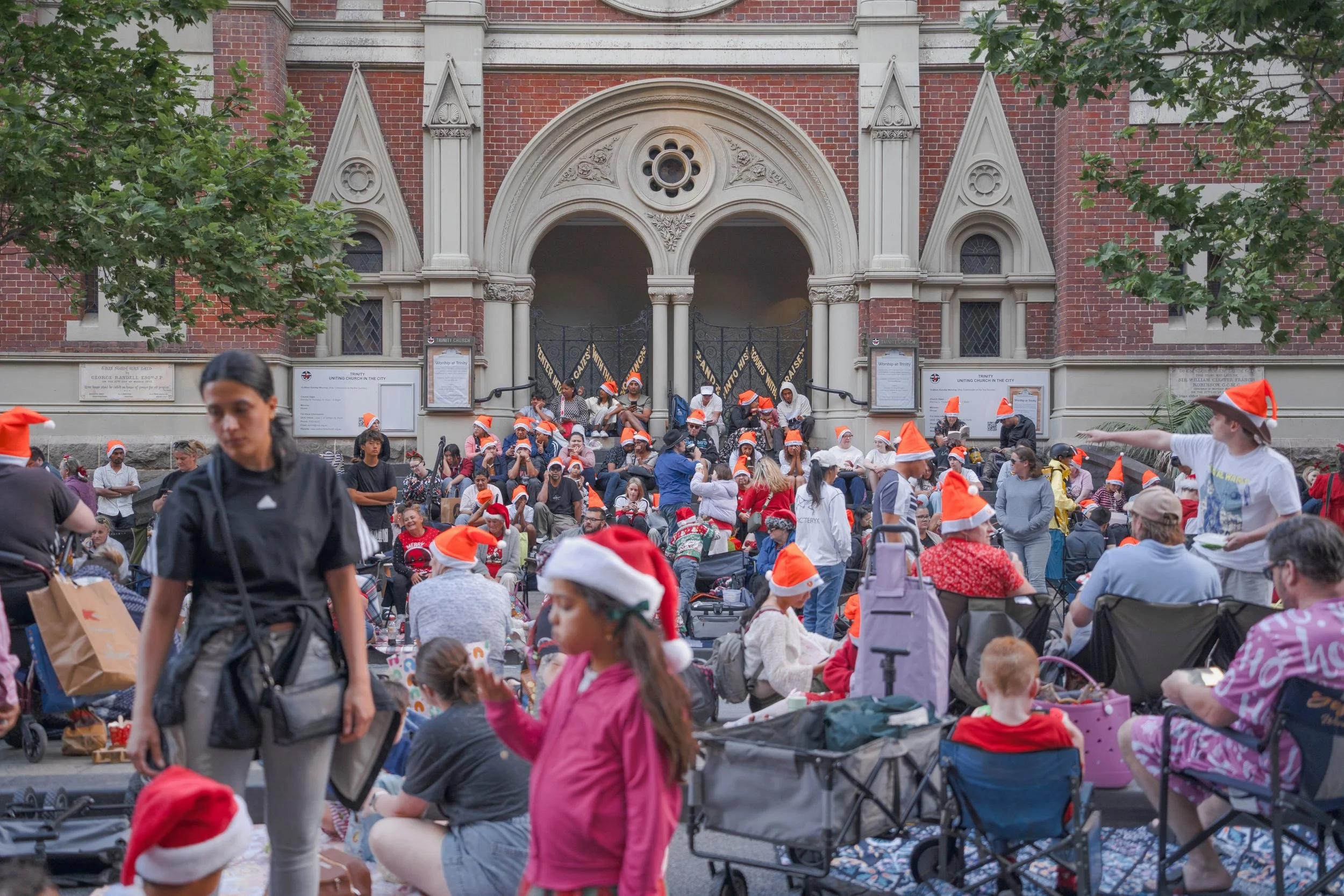 Crowd of people wearing Santa hats gathered outside a historic church.