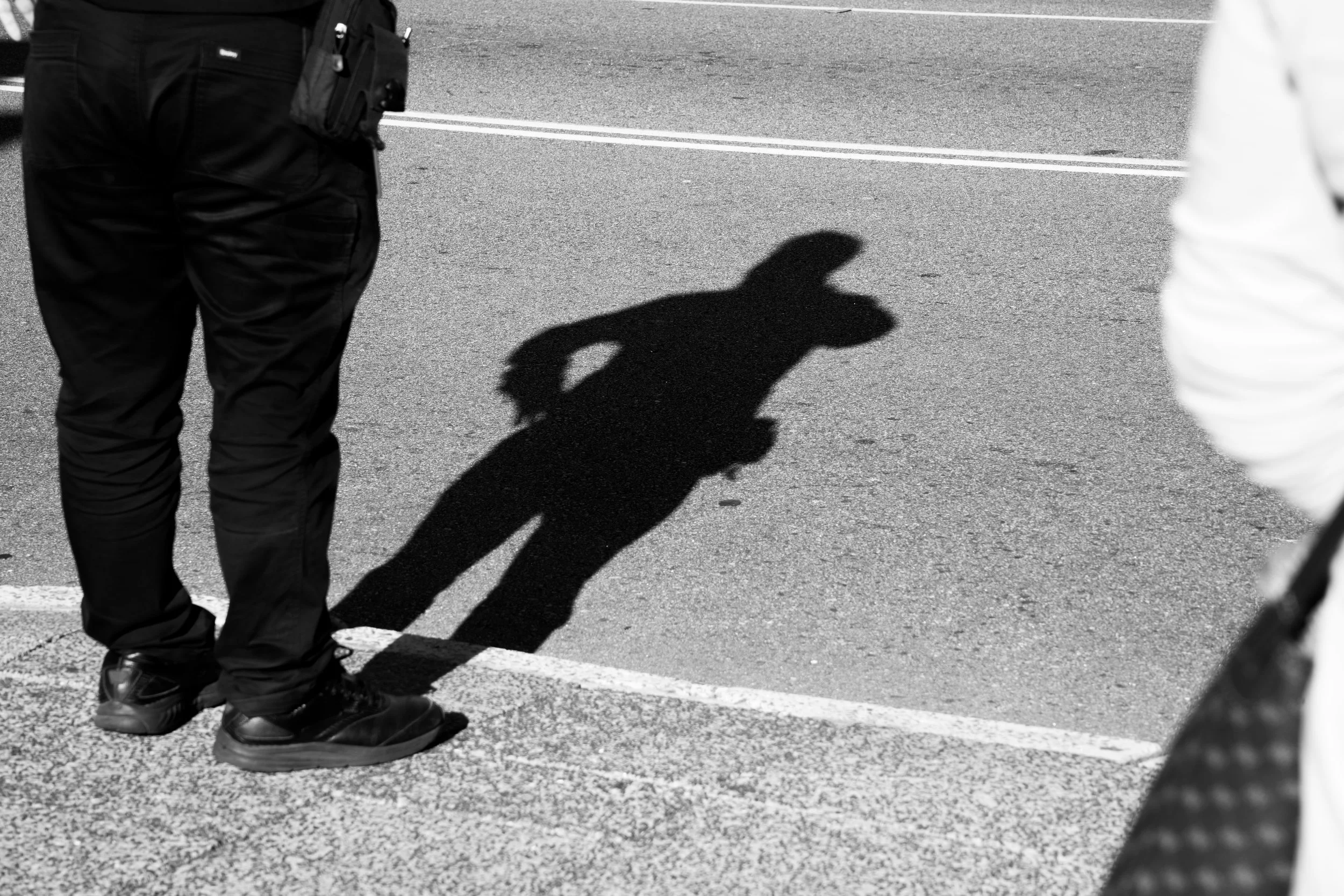Shadow of a person on an empty street, partially visible police officer standing nearby.