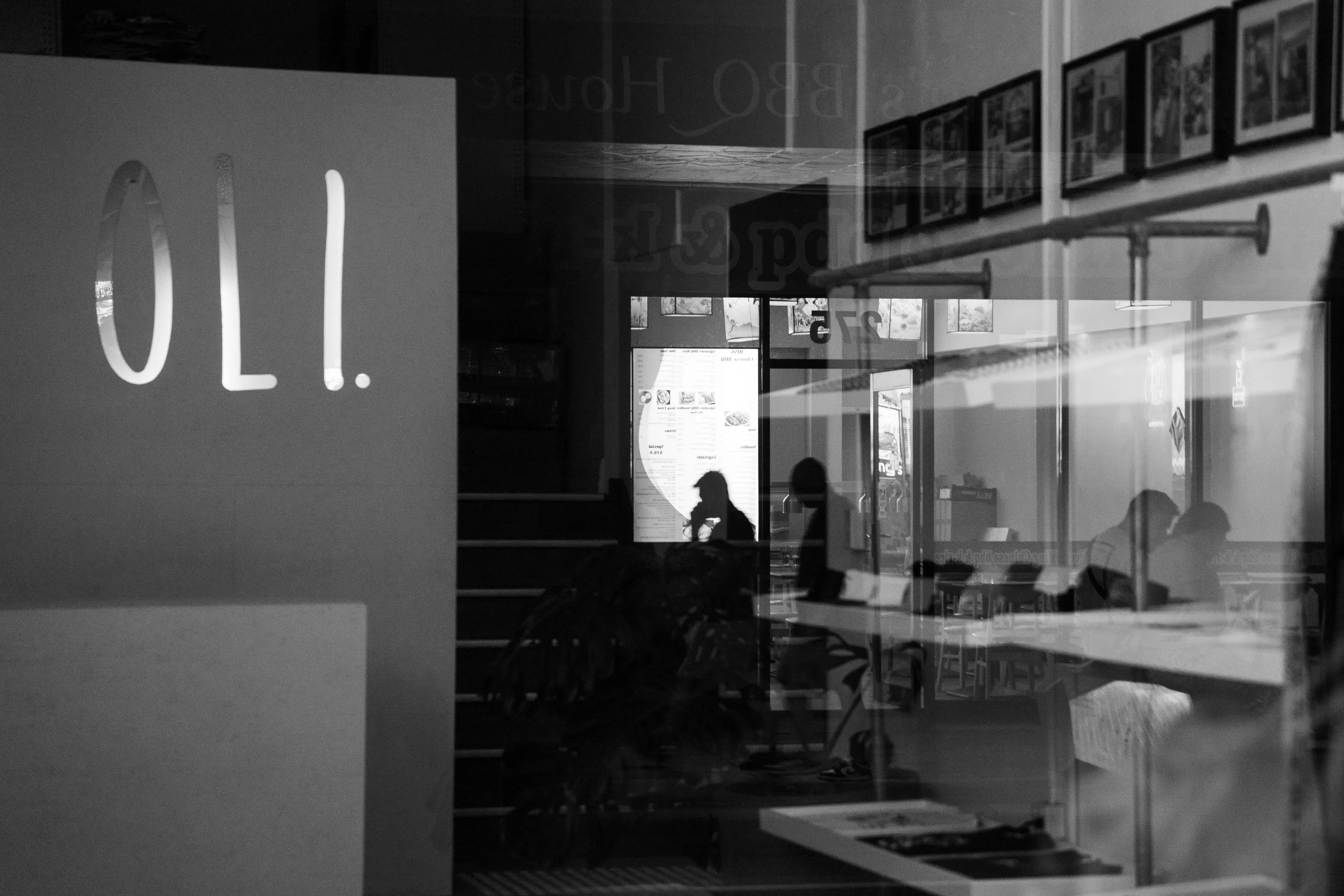 Reflection of people inside a cafe or restaurant through a window with a sign reading '10.00' in the foreground.