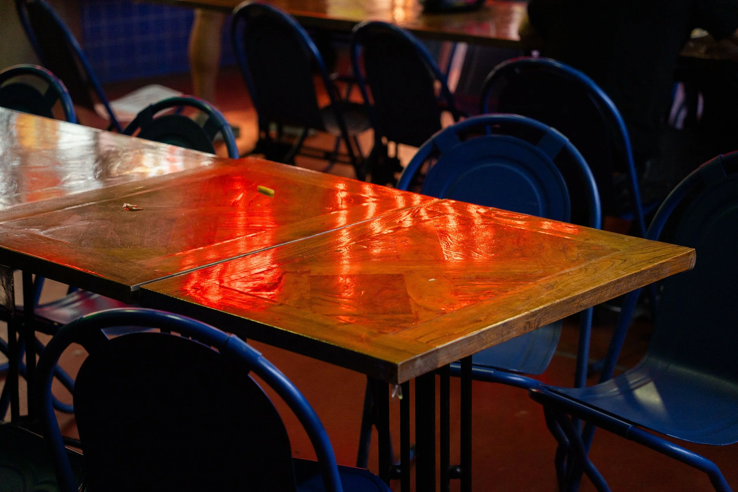 Empty wooden table with blue chairs around, dimly lit restaurant or bar interior.