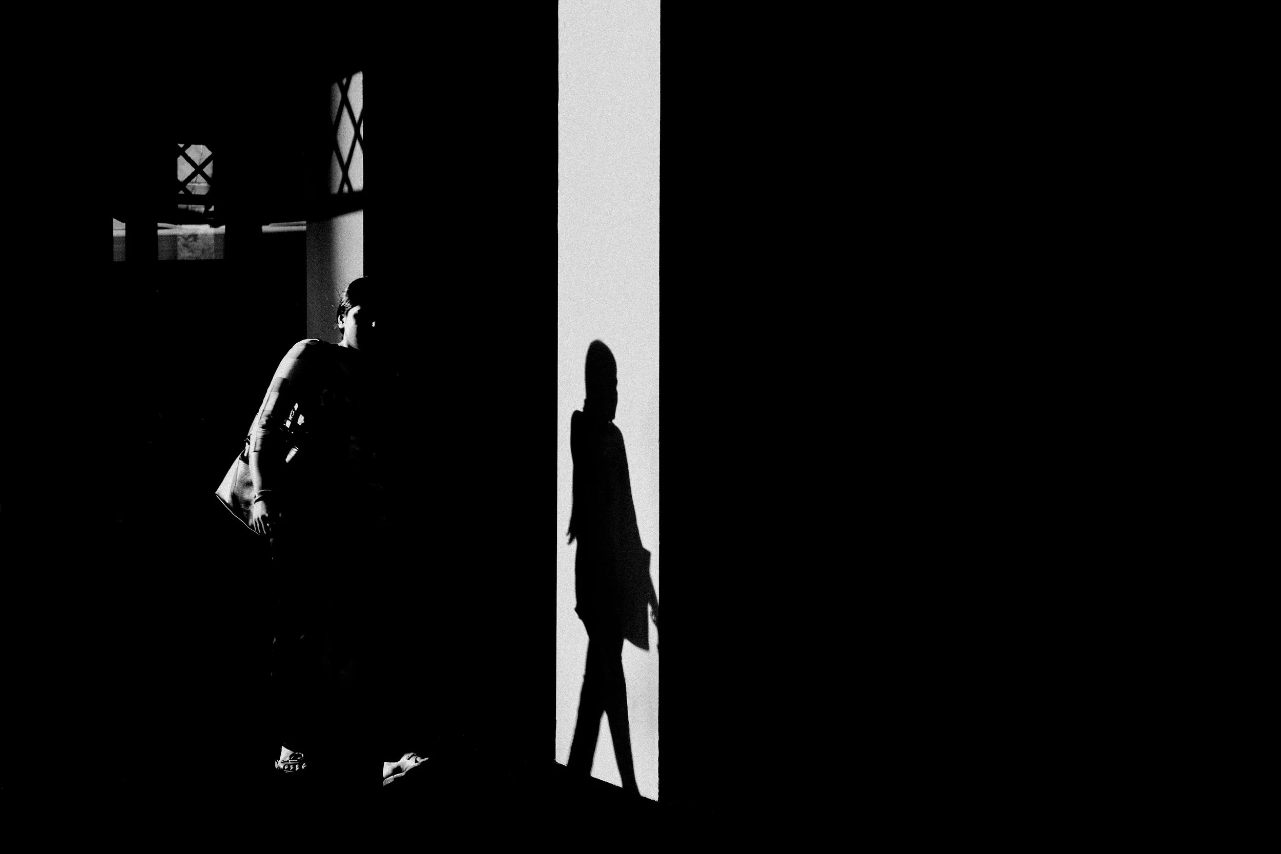 Shadowed silhouette of a woman walking through an illuminated door opening, with her shadow cast on the wall.