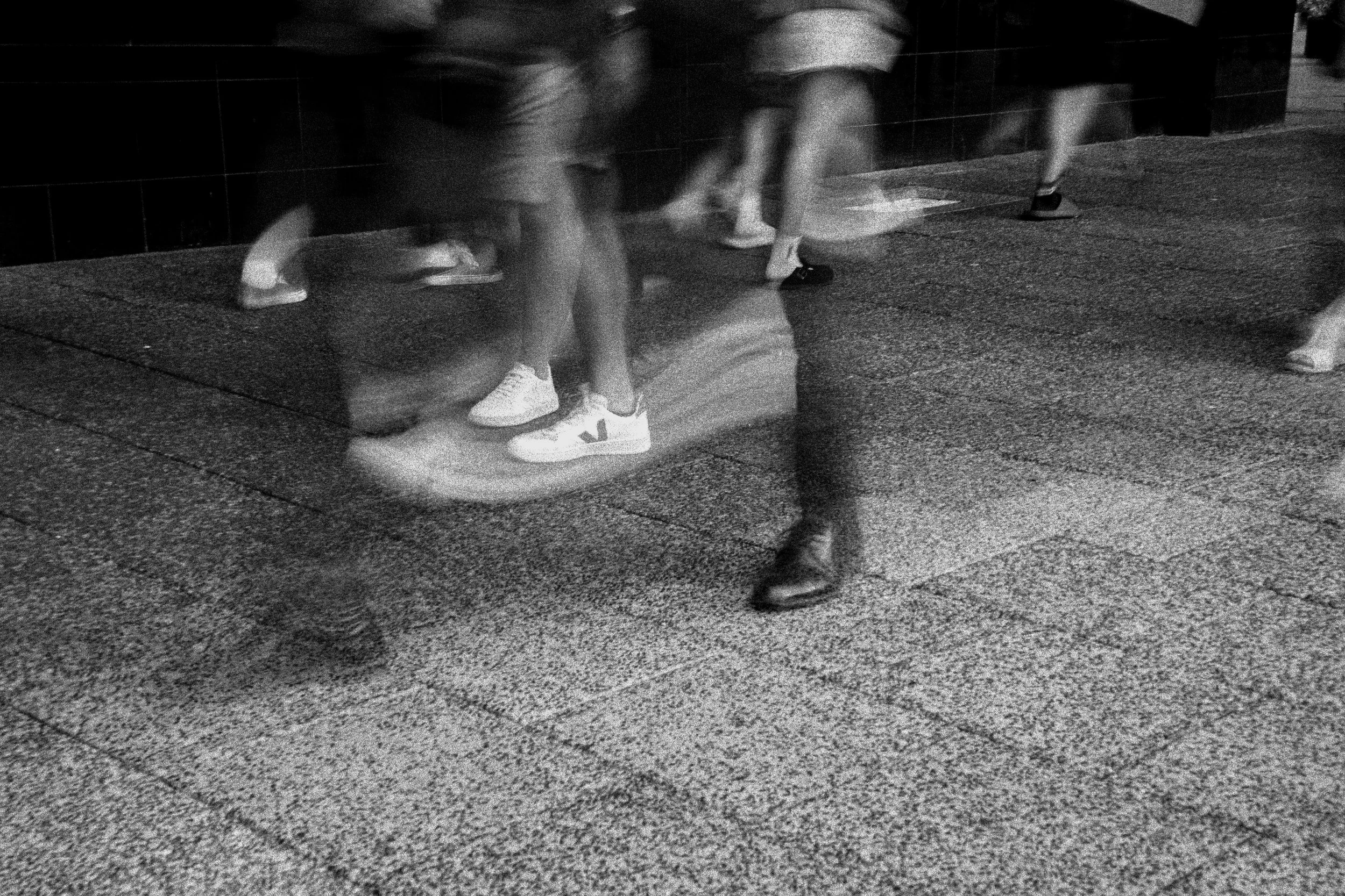 Blurred black and white image of people walking on a sidewalk at night.